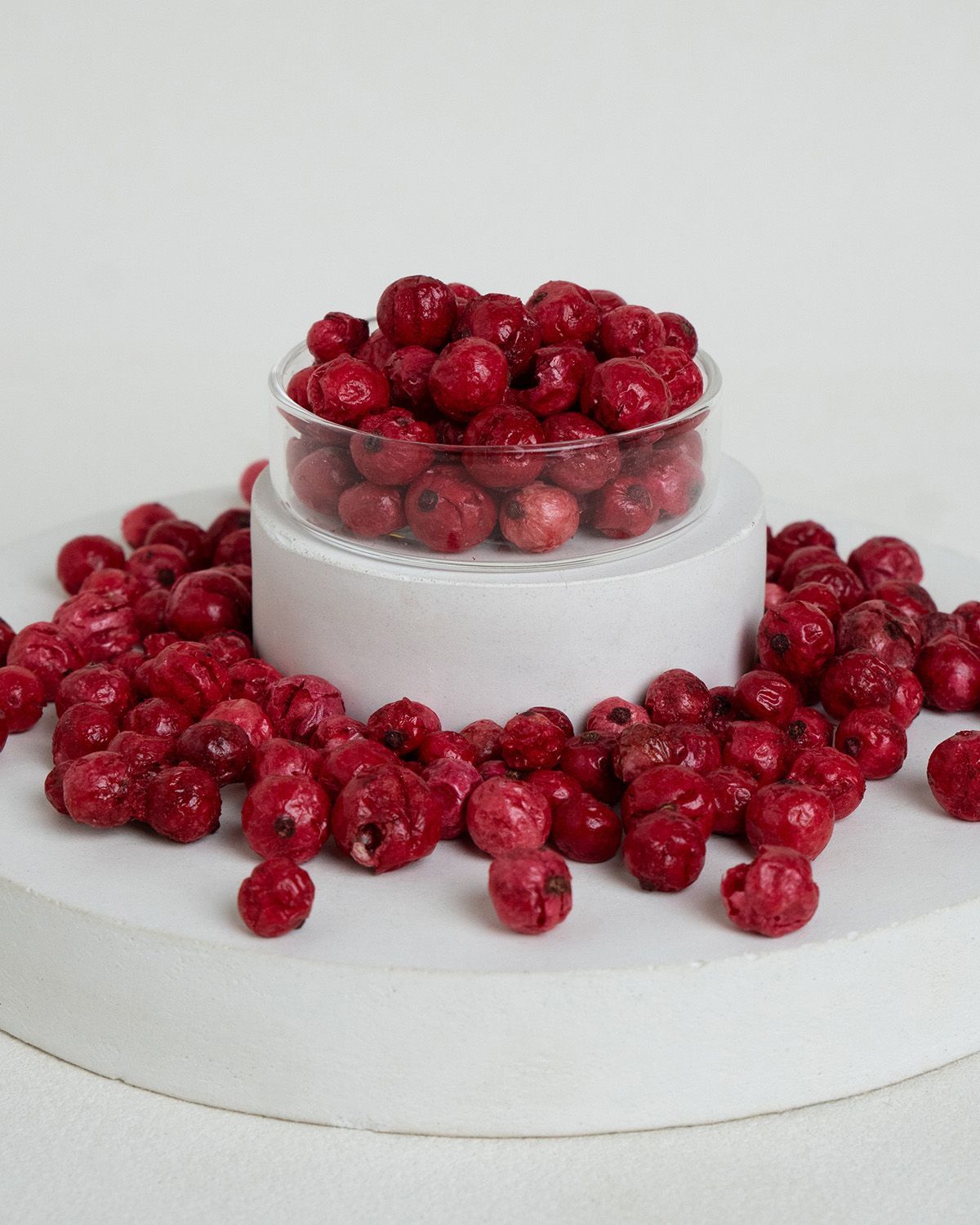 Gefriergetrocknete rote Johannisbeeren in einer Glasschale und verstreut auf einem Podest.