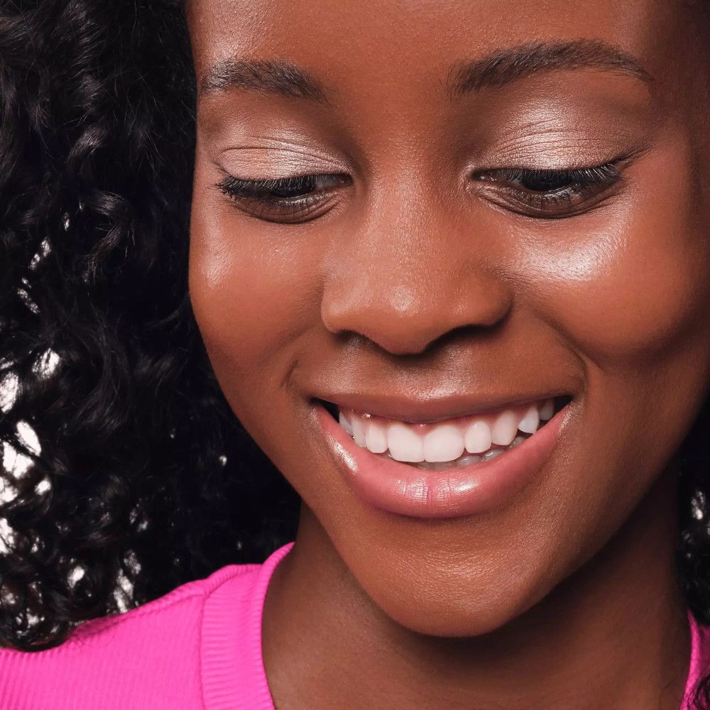 Nahaufnahme einer lächelnden Frau mit Lidschatten auf den Augenlidern. Rosa Oberteil.