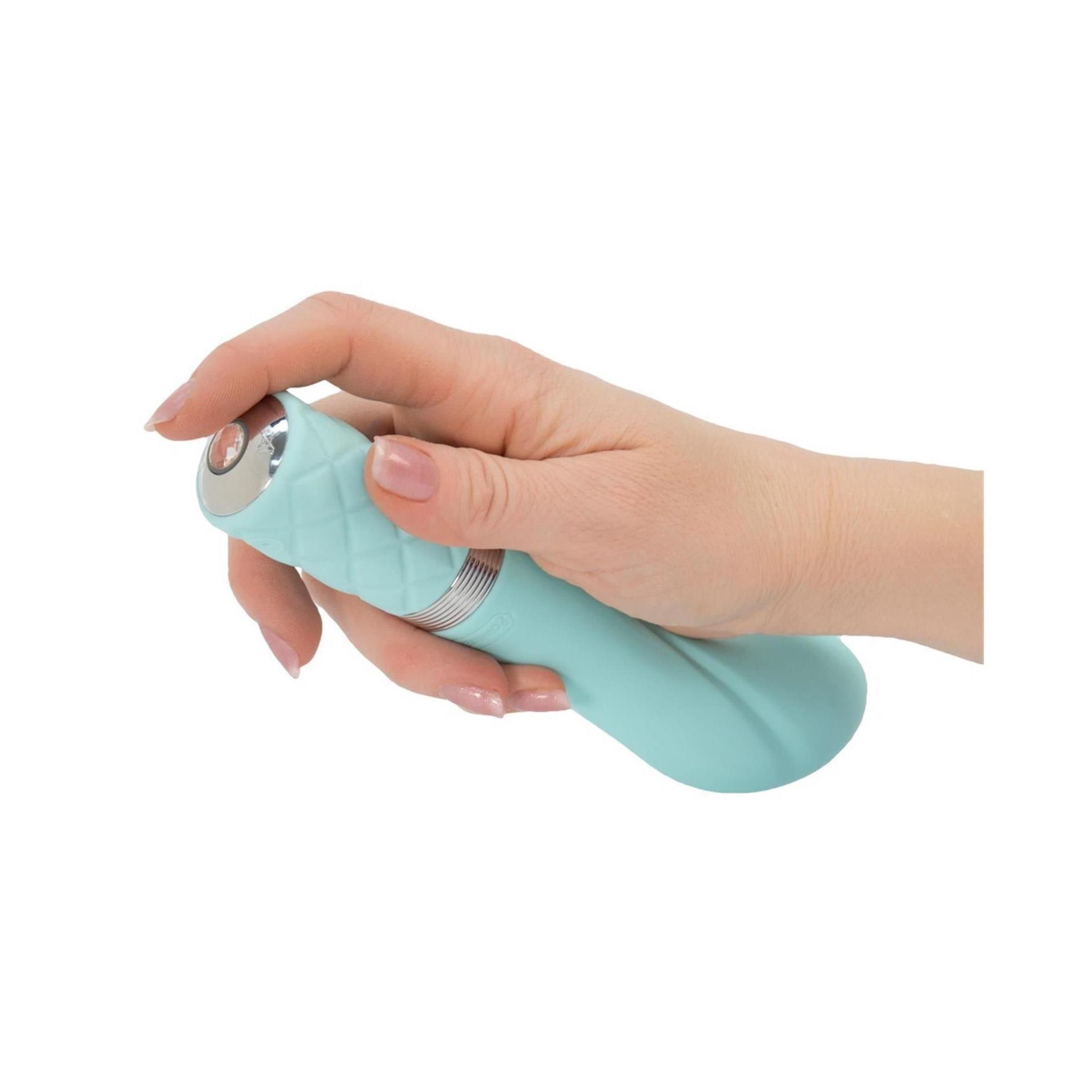 Hand hält türkisfarbenen Vibrator. Der Griff hat ein Rautenmuster. Silberfarbener Ring am Übergang.