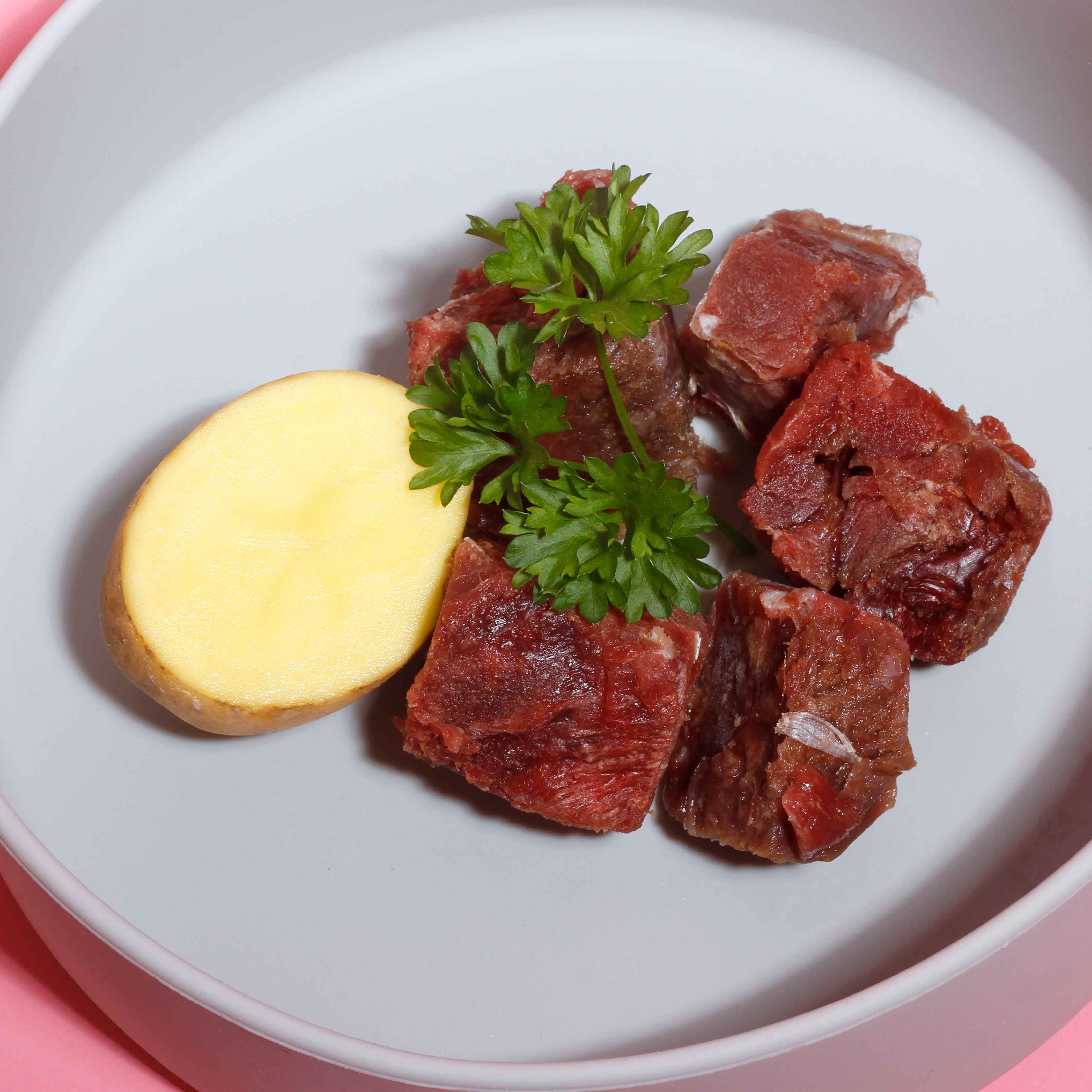 In einer Schale: Kartoffelscheibe, Petersilie und Fleischstücke. Rosa Hintergrund.