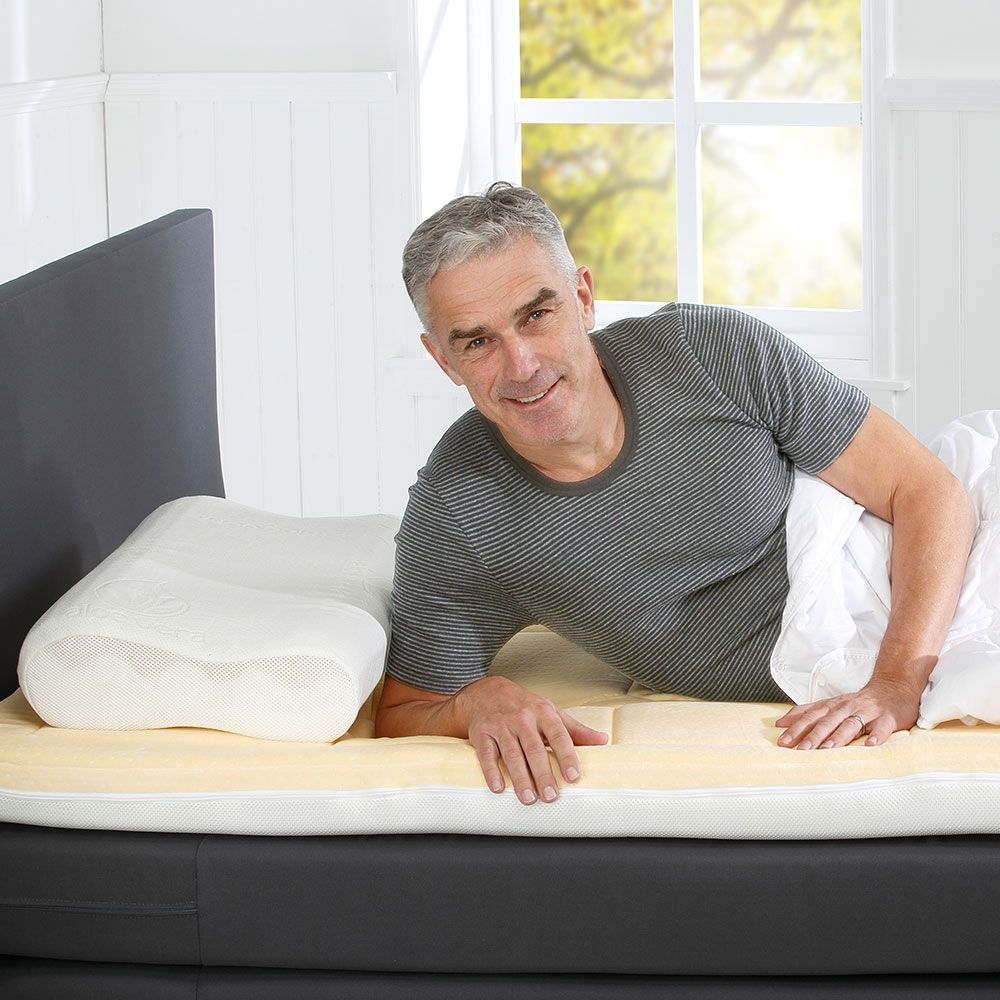 Mann liegt auf Bett mit Matratzenauflage und Kissen.