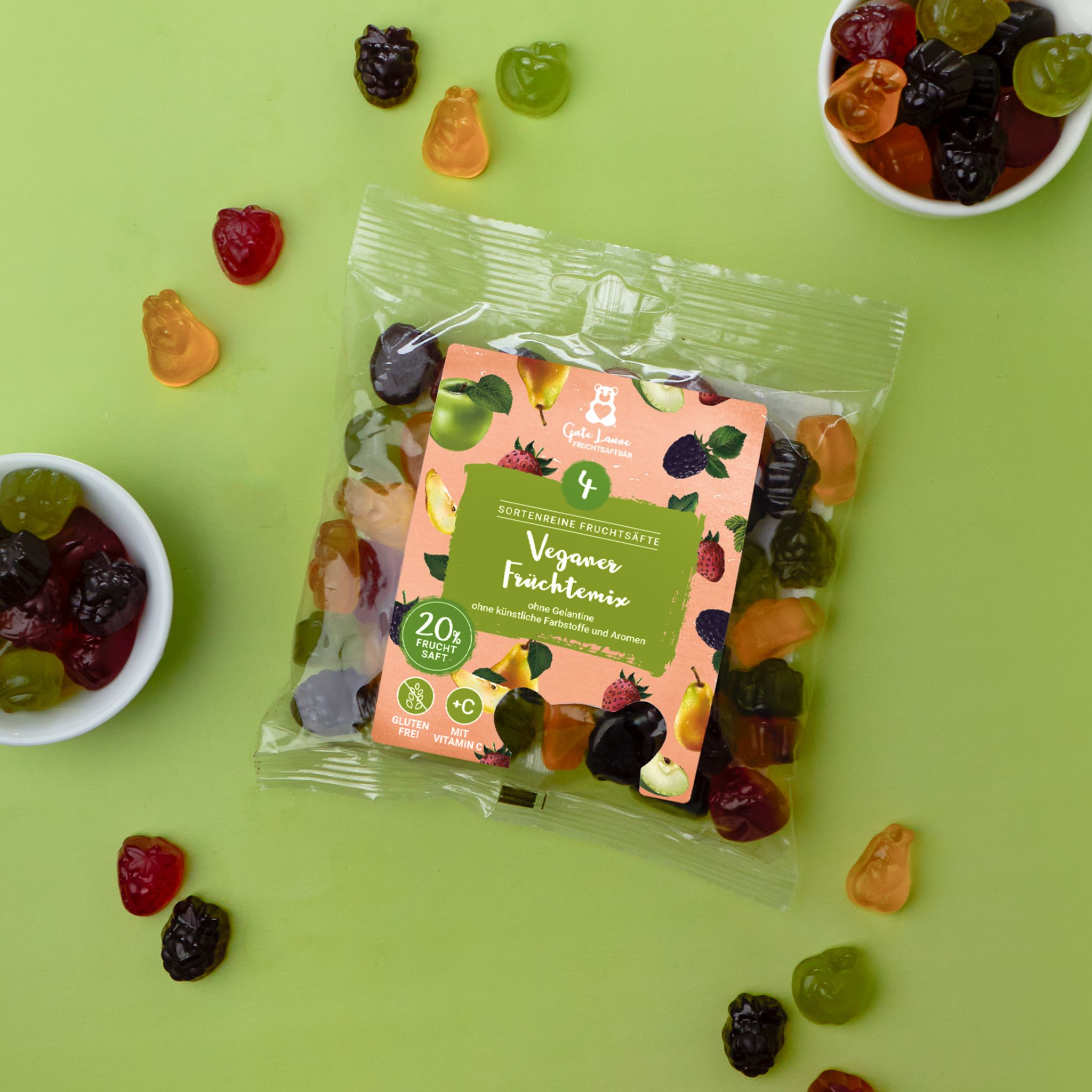 Transparente Tüte mit Fruchtgummis und Aufdruck. Auf dem Etikett steht "Veganer Früchtemix". Einige Gummis liegen verstreut.