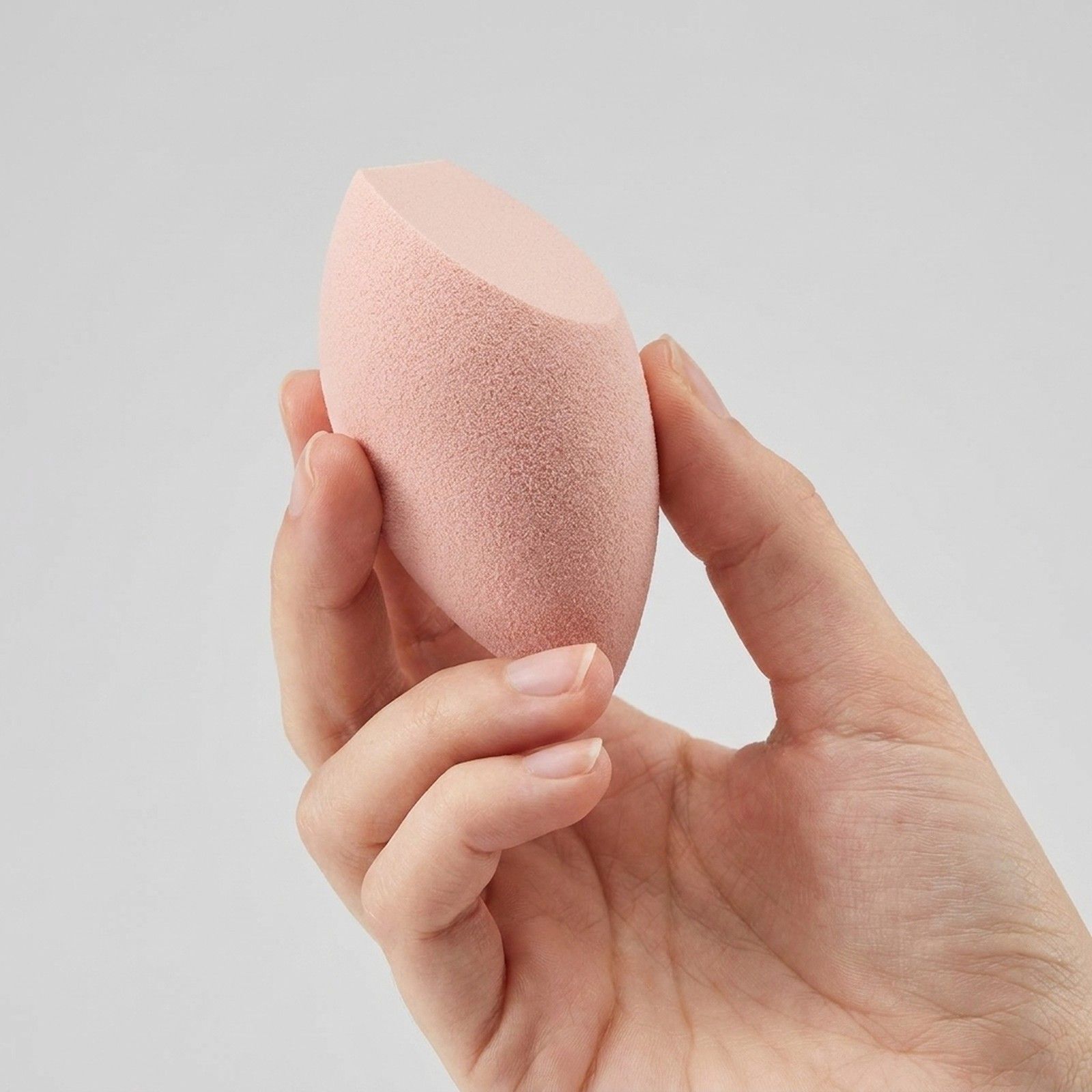 Eine Hand hält einen rosafarbenen Make-up-Schwamm mit abgeschrägter Spitze.