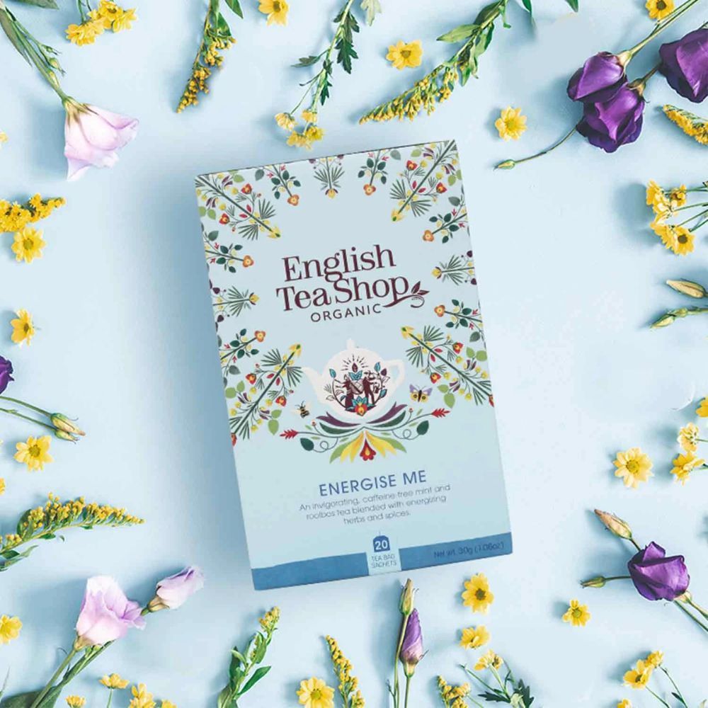 Hellblaue Schachtel mit floralem Muster und Text. Aufschrift: English Tea Shop, ORGANIC, Energise Me. Umgeben von Blumen.