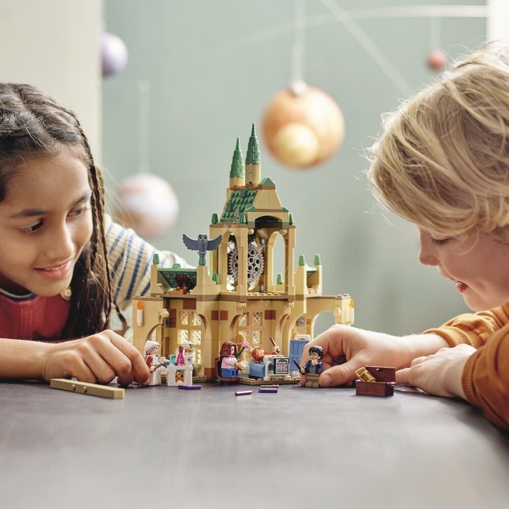 Due bambini giocano con un set LEGO Harry Potter Ala dell'Infermeria di Hogwarts. Il set è allestito su un tavolo. I bambini interagiscono con i personaggi e l'edificio. Il set include l'edificio dell'Ala dell'Infermeria di Hogwarts con orologio, personaggi e accessori.