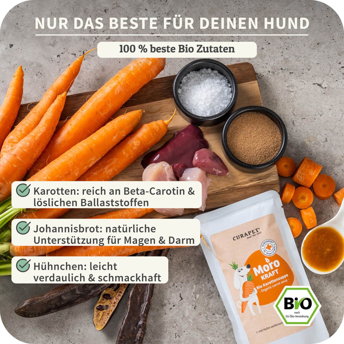Zutaten auf Holzbrett: Karotten, Johannisbrot, Hühnchen, Salz. Beutel: CURAPET, Moro Kraft, Bio Karottensuppe. Bio-Siegel.