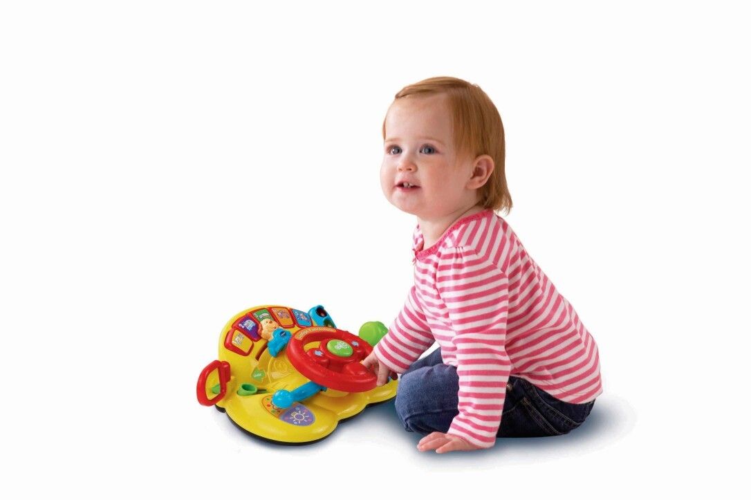 Kleinkind sitzt und spielt mit gelbem Spielzeug-Lenkrad. Rotes Lenkrad, gelbe Basis.