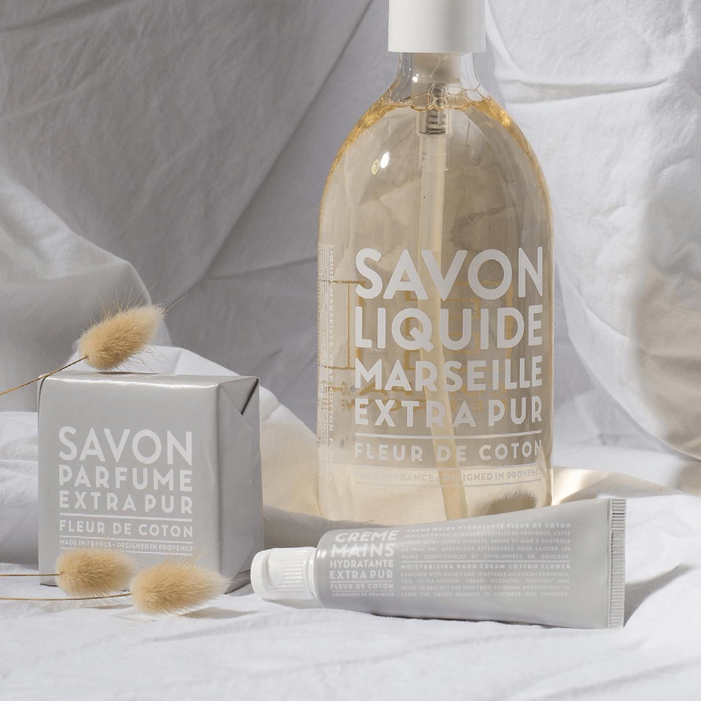 Flüssigseife und Handcreme in neutralen Verpackungen, mit getrockneten Gräsern dekoriert.