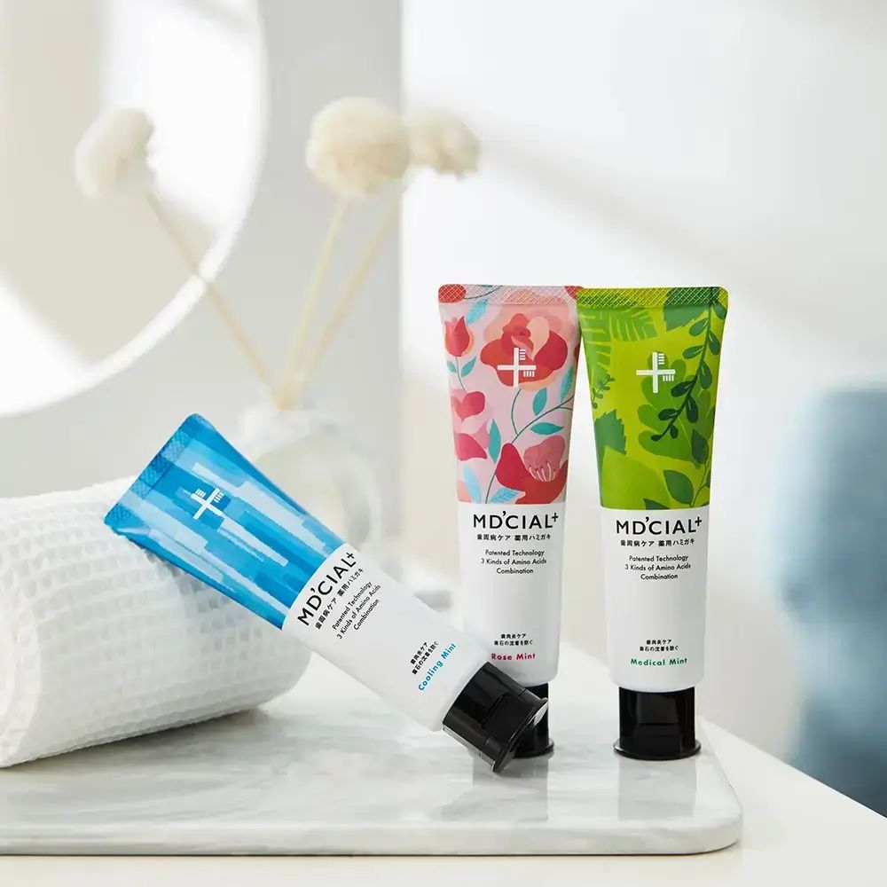 Drei Zahncreme-Tuben. Blau, rosa und grün. Schriftzug MD'CIAL+. Auf weißem Handtuch liegend.