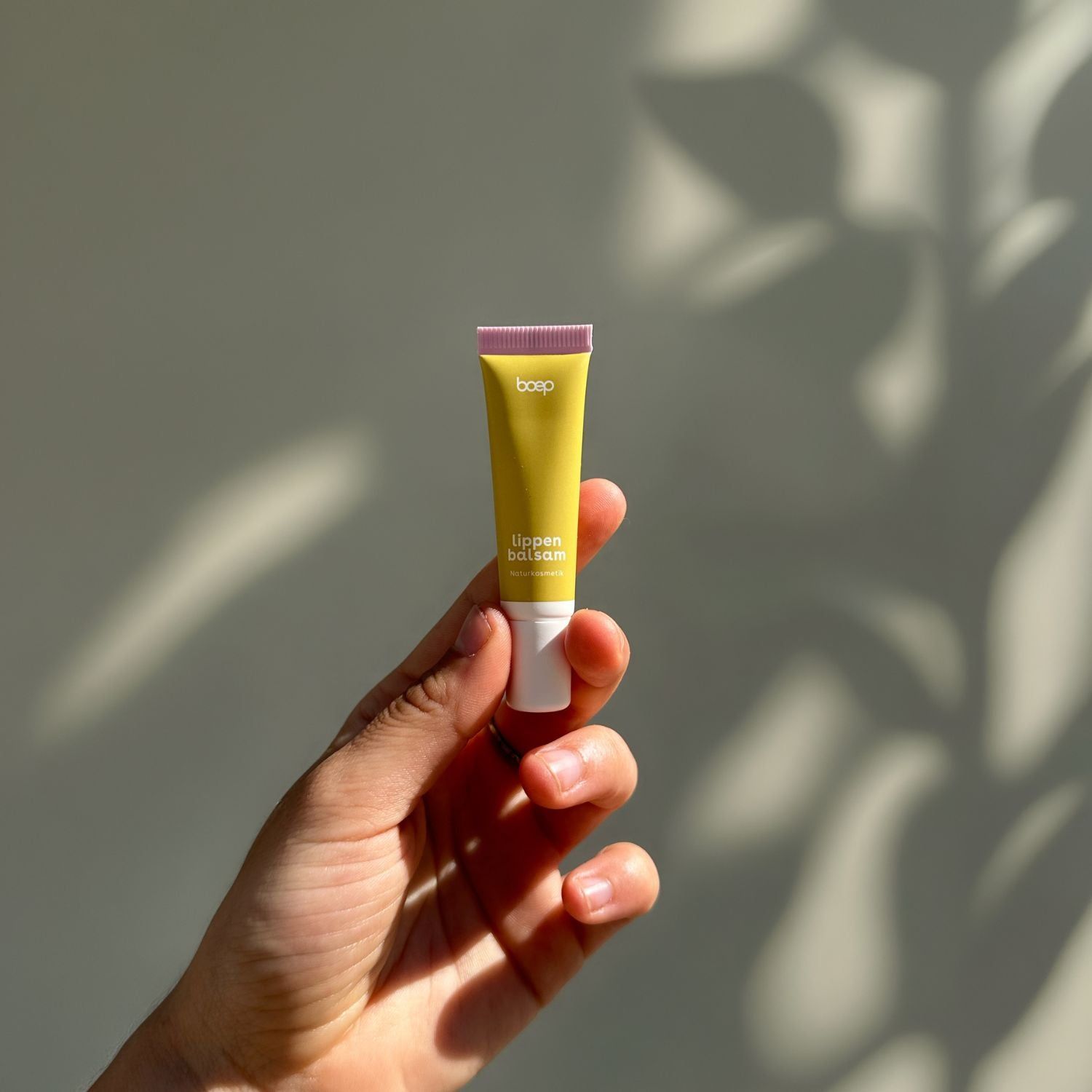 Hand hält eine kleine gelbe Tube Lippenbalsam mit weißem und pinkem Verschluss.