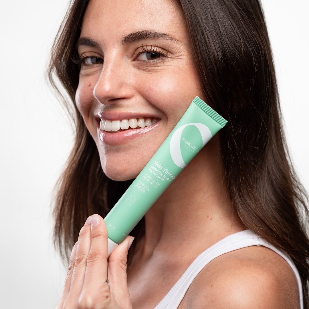 Frau hält eine grüne Tube. Auf der Tube steht "Skin Therapy". Sie lächelt.