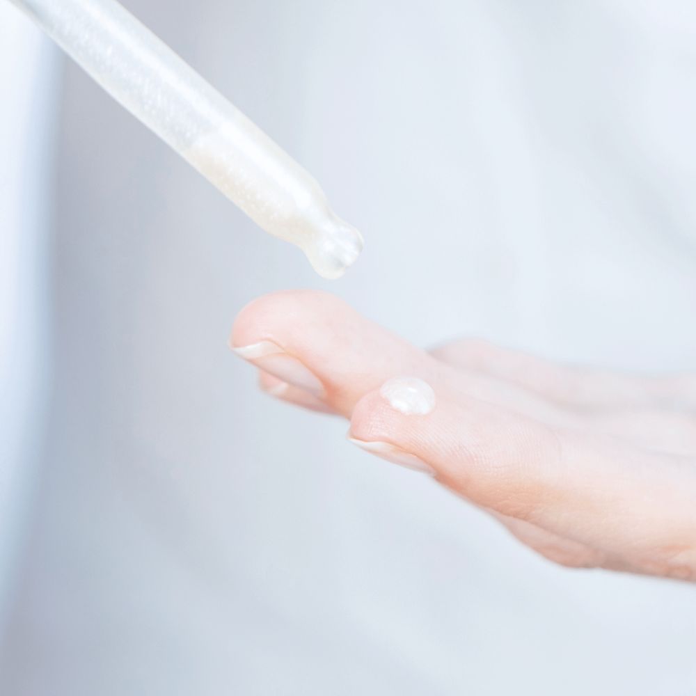 Serum wird mit einer Pipette auf einen Finger aufgetragen. Auf dem Finger befindet sich ein Tropfen Serum.