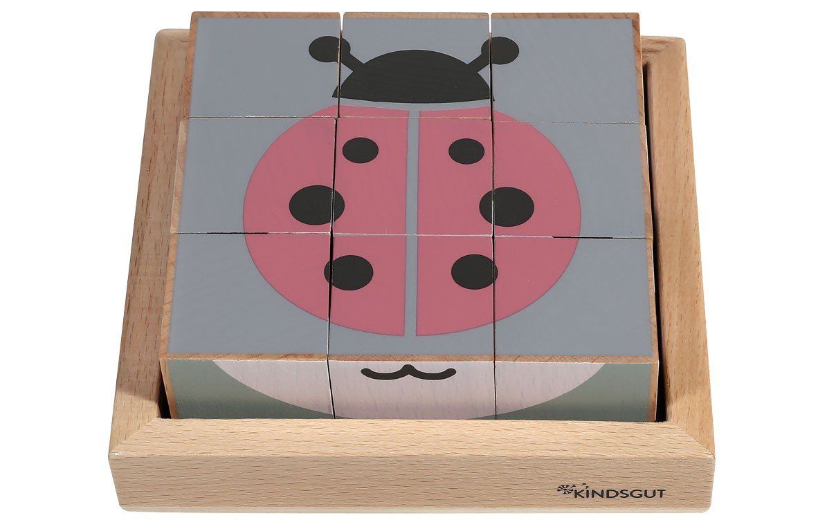Holzwürfel-Puzzle mit Marienkäfer-Motiv. Neun Würfel bilden ein Bild in einem Holzrahmen. Rosa, grau und schwarz. Logo Kindsgut.