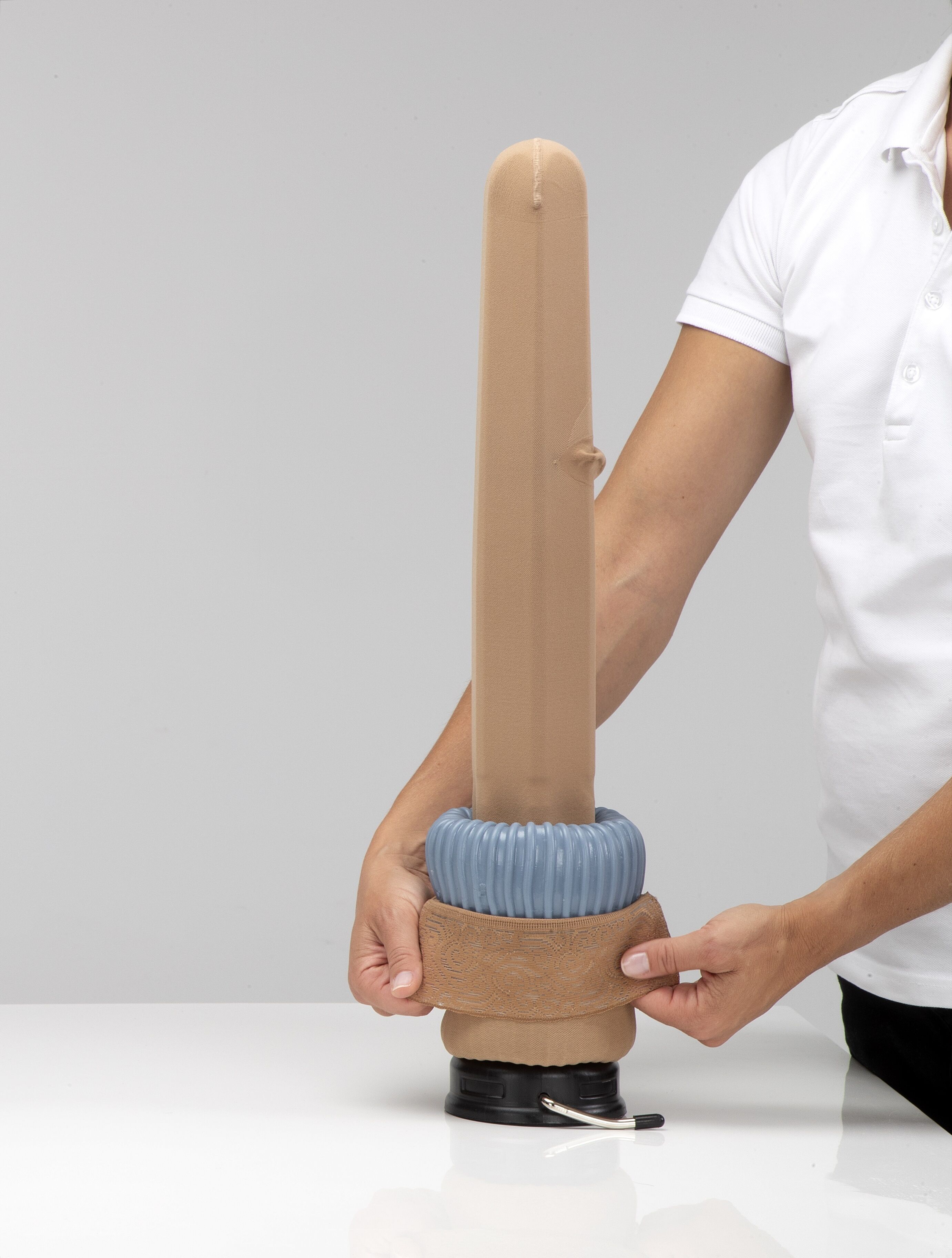 Person hält Anziehhilfe mit Kompressionsstrumpf. Anziehhilfe und Strumpf sind beige. Hintergrund weiß.