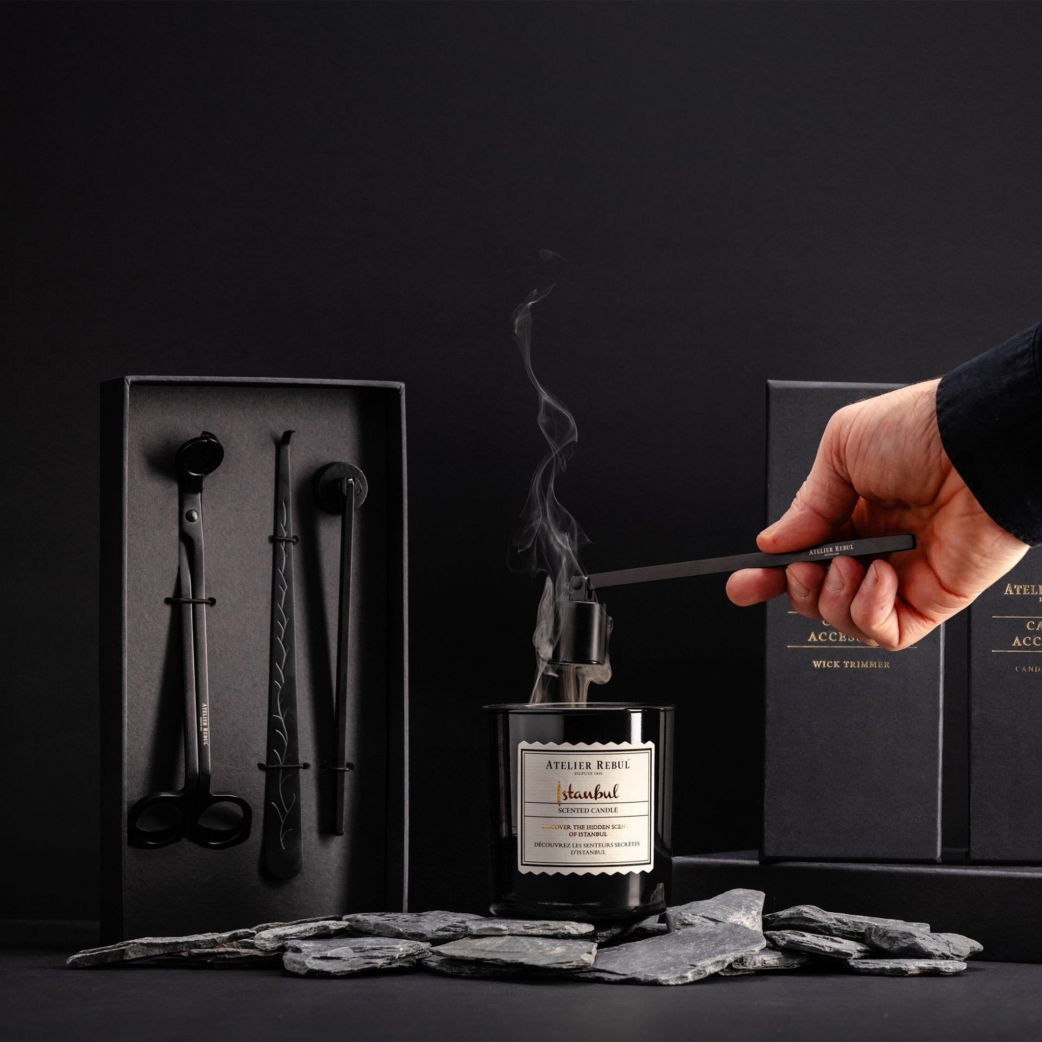 Ein Atelier Rebul Kerzenpflege-Set mit schwarzer Kerze, Dochtschere, Dochtheber und Löscher.