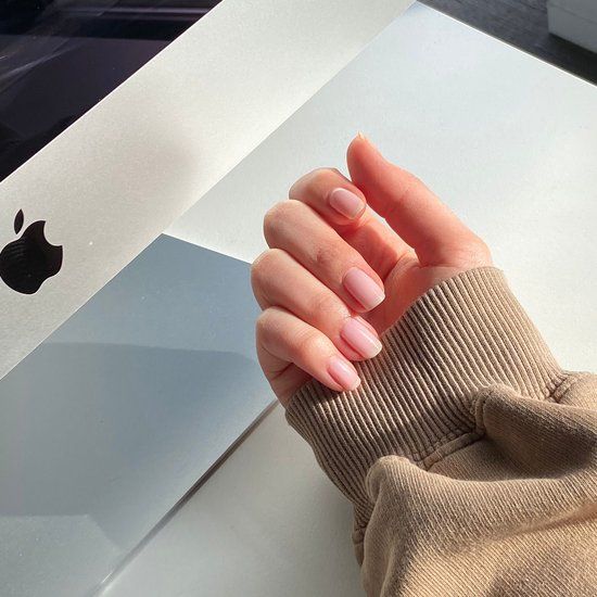 Hand mit lackierten Nägeln. Hellrosa Farbe. Abgerundete Form. Auf einem Laptop.