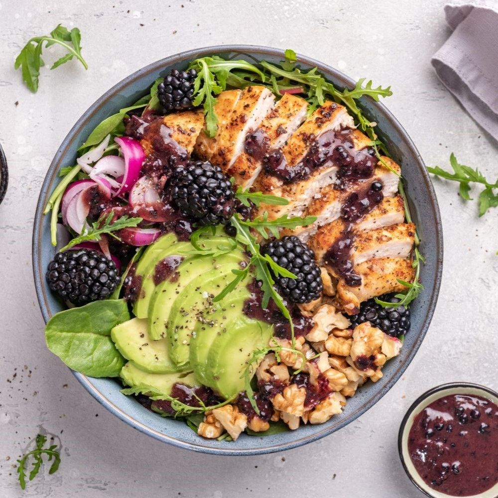 Salatschüssel mit Hähnchen, Avocado, Brombeeren, Walnüssen und Dressing. Frische Zutaten, appetitlich angerichtet.