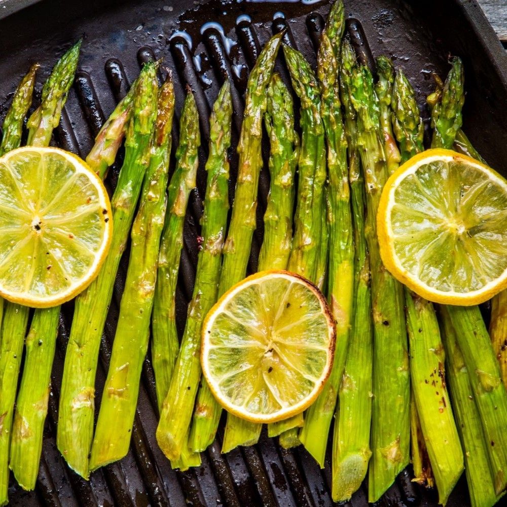 Gegrillter Spargel mit Zitronenscheiben. Auf schwarzem Grillrost. Grüne Spargelstangen, gelbe Zitronenscheiben.