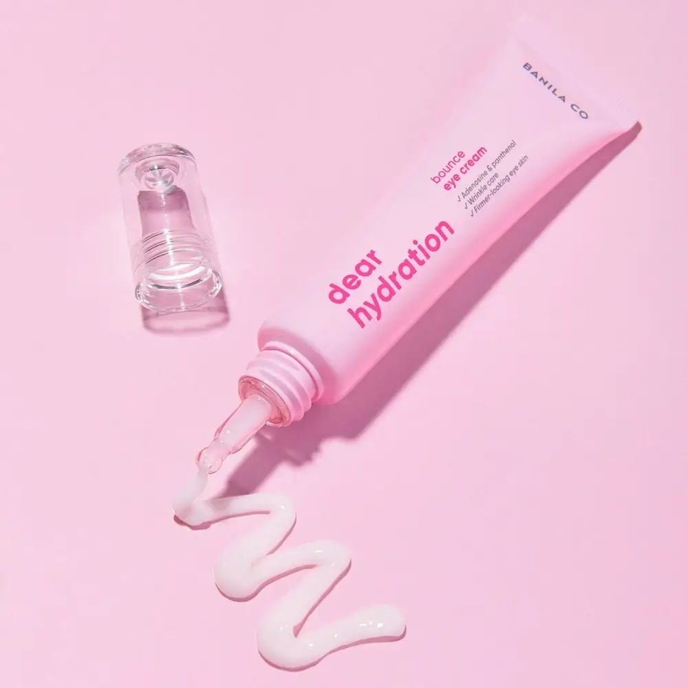 Rosa Tube mit weißer Creme. Aufschrift: BANILA CO, Dear Hydration, Bounce Eye Cream. Transparenter Applikator daneben.