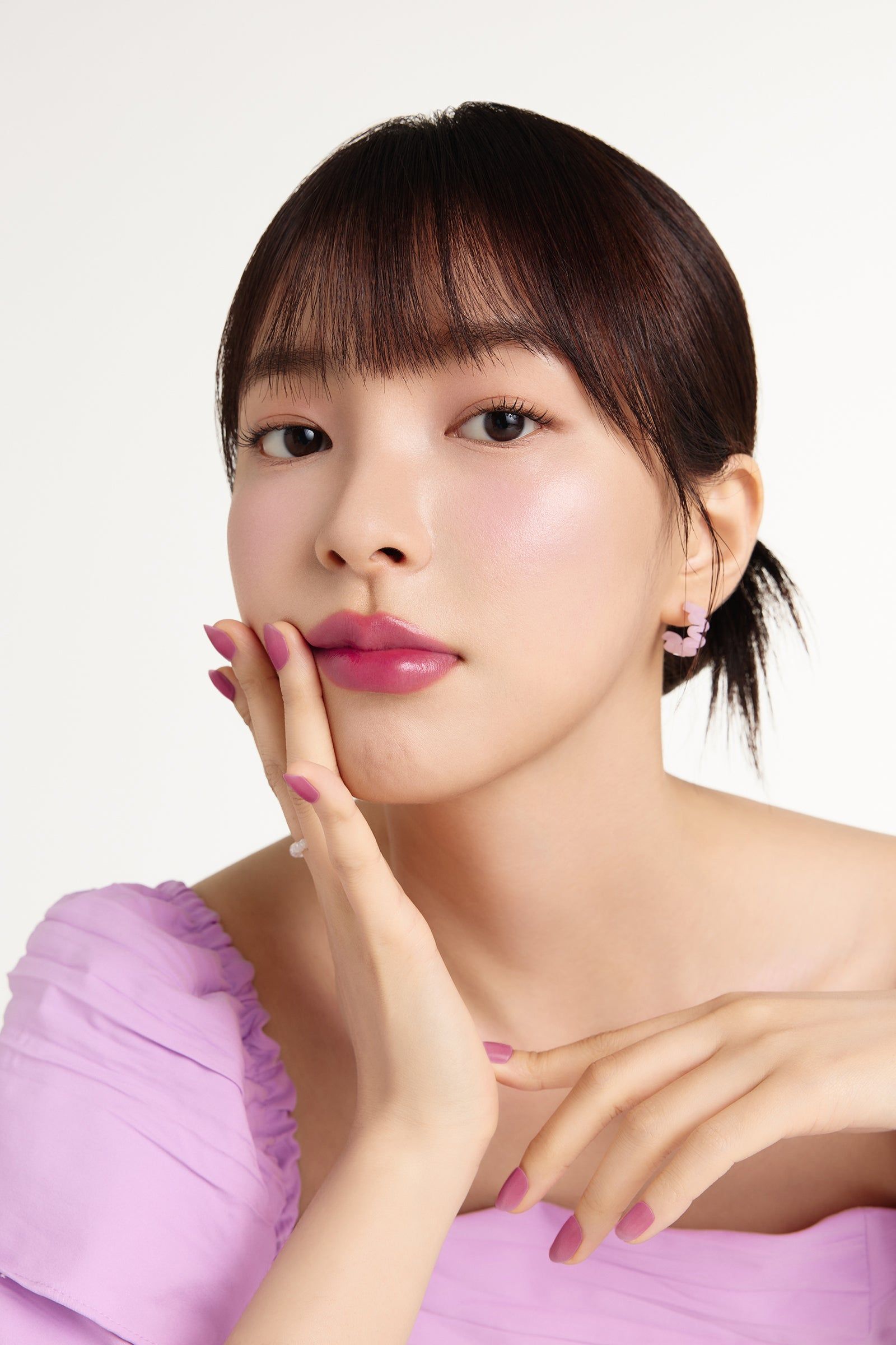 Porträt einer Frau mit rosa Lippenstift. Sie berührt ihre Lippen mit einem Finger.