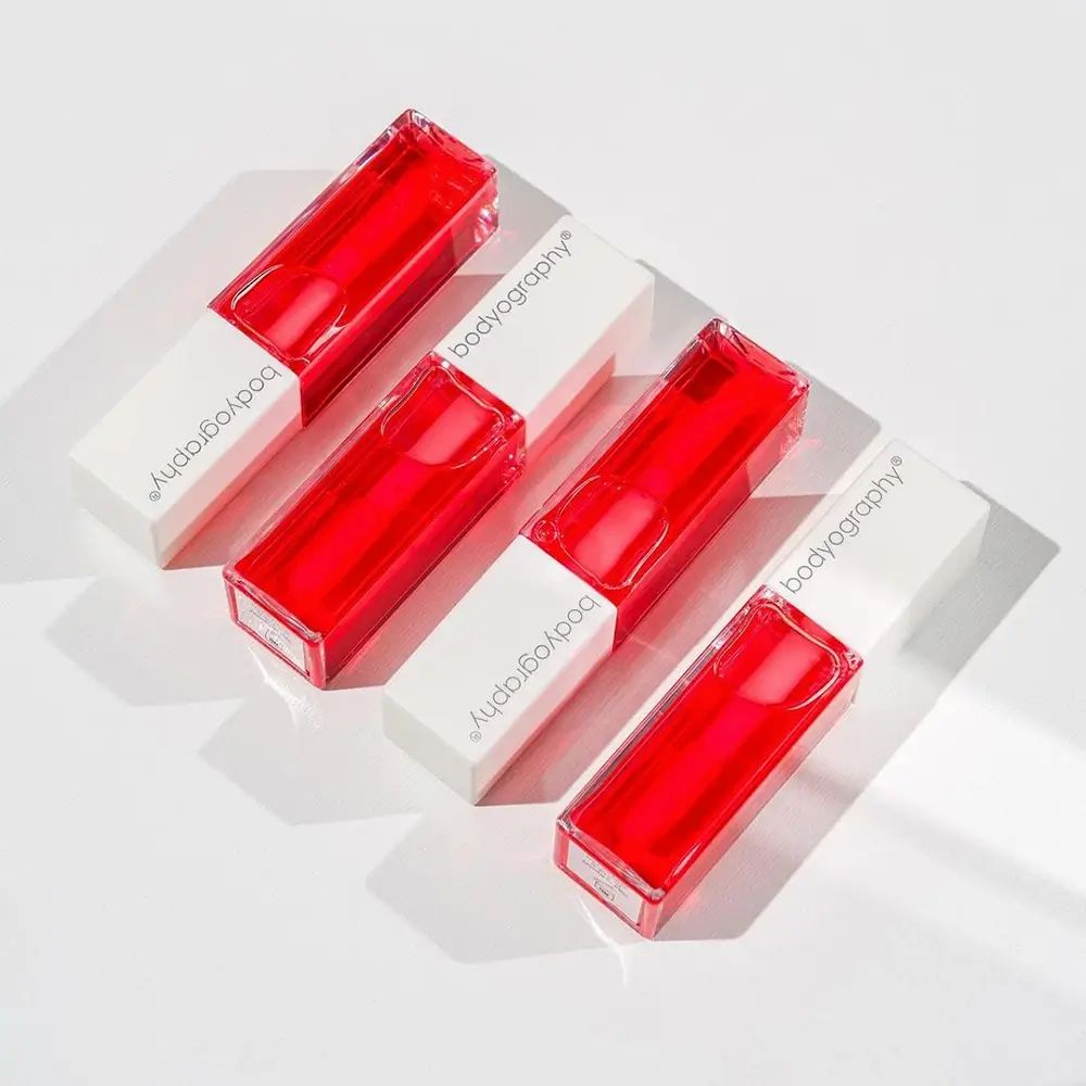 Vier Lipgloss-Fläschchen mit rotem Inhalt und weißem Deckel. Auf den Deckeln steht Bodyography.