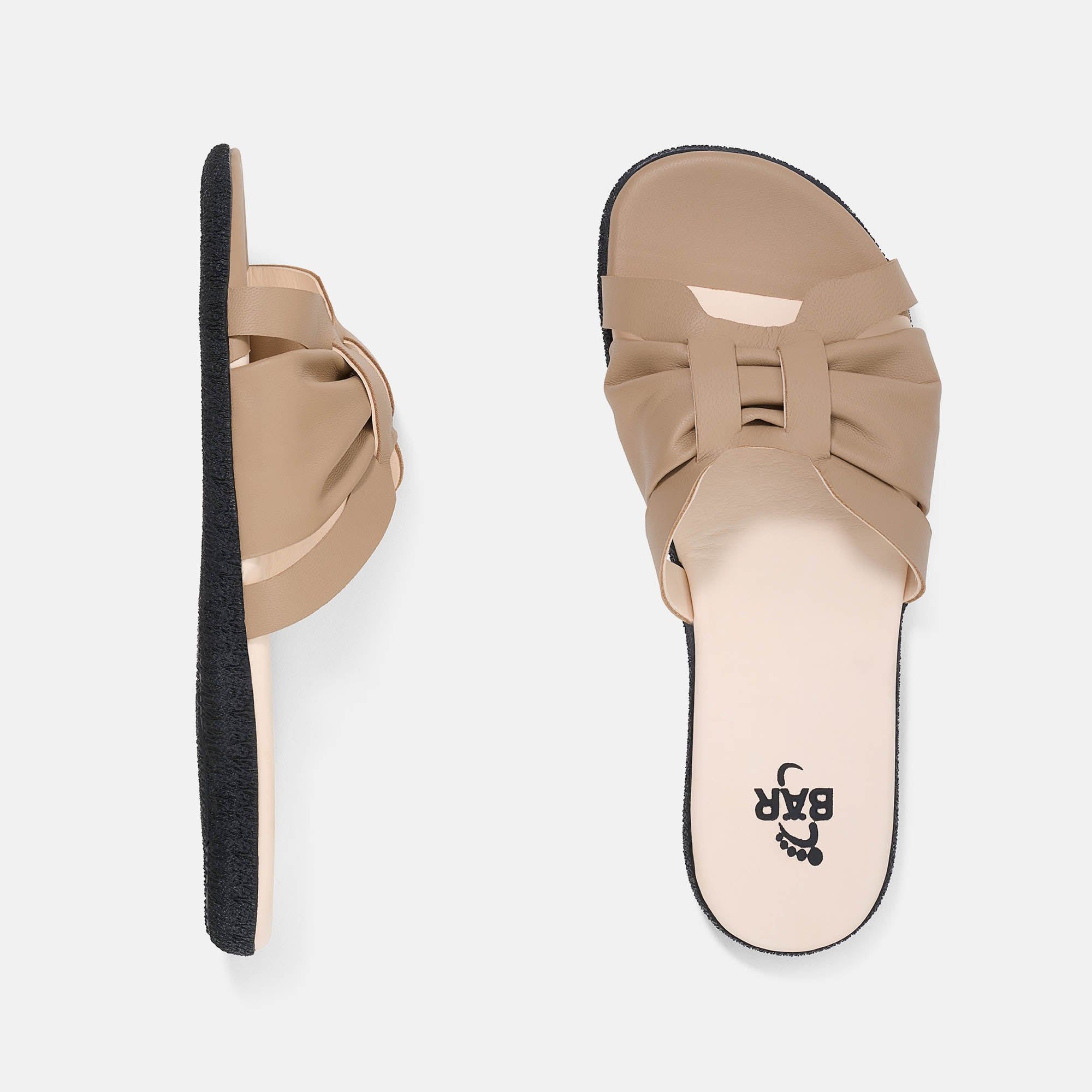 Zwei Pantoletten, eine von der Seite, eine von oben. Beige, Obermaterial mit Faltenwurf, schwarze Sohle. Marke BÄR.