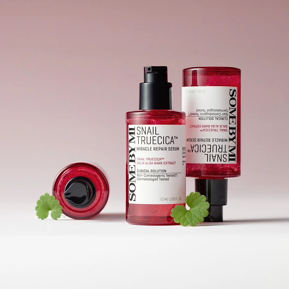 Drei rote Serumflaschen mit schwarzem Deckel. Produktname und Inhaltsstoffe auf den Etiketten. Grüne Blätter.