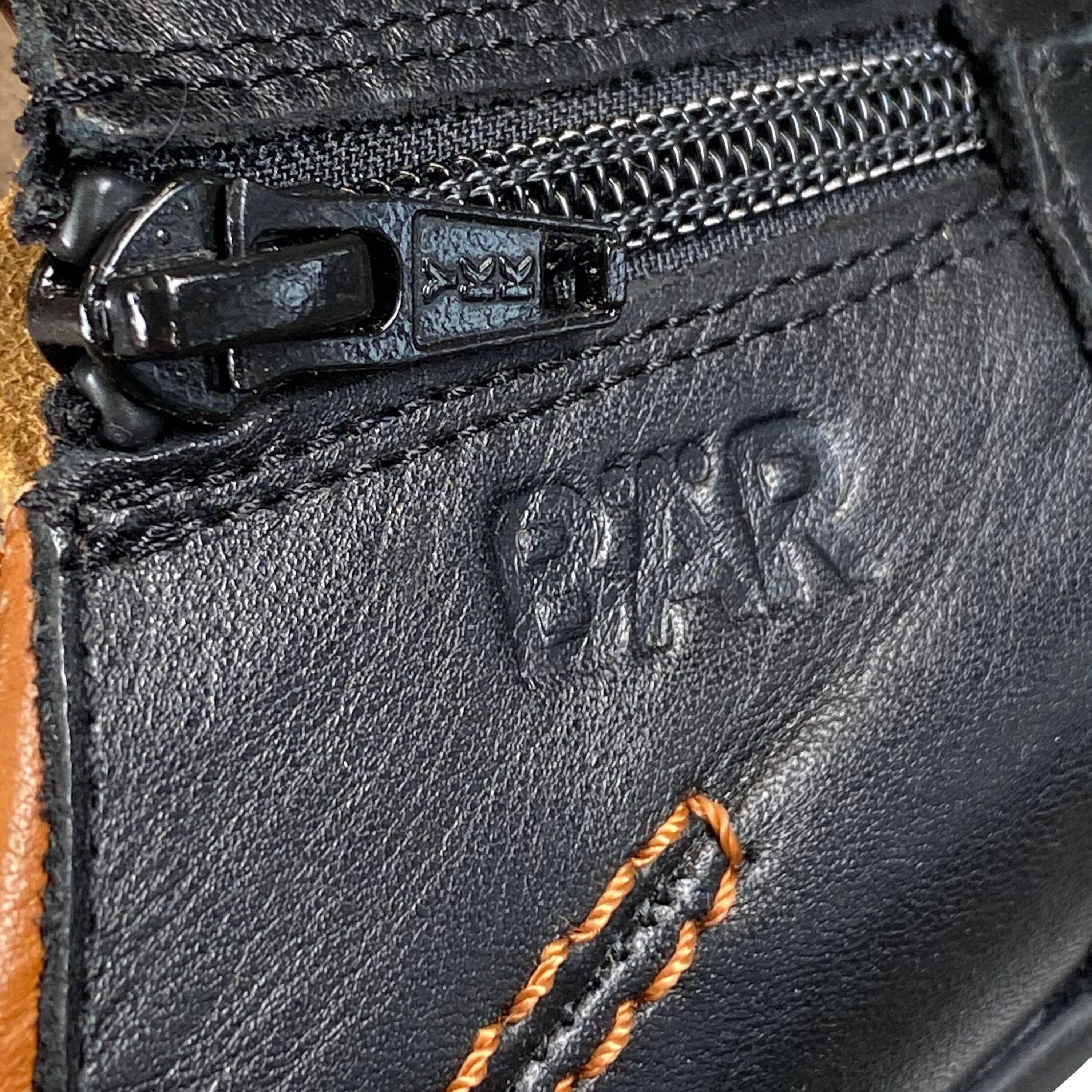 Nahaufnahme des BÄR-Logos auf einem schwarzen Lederschuh. Reißverschluss und braune Nähte sichtbar.