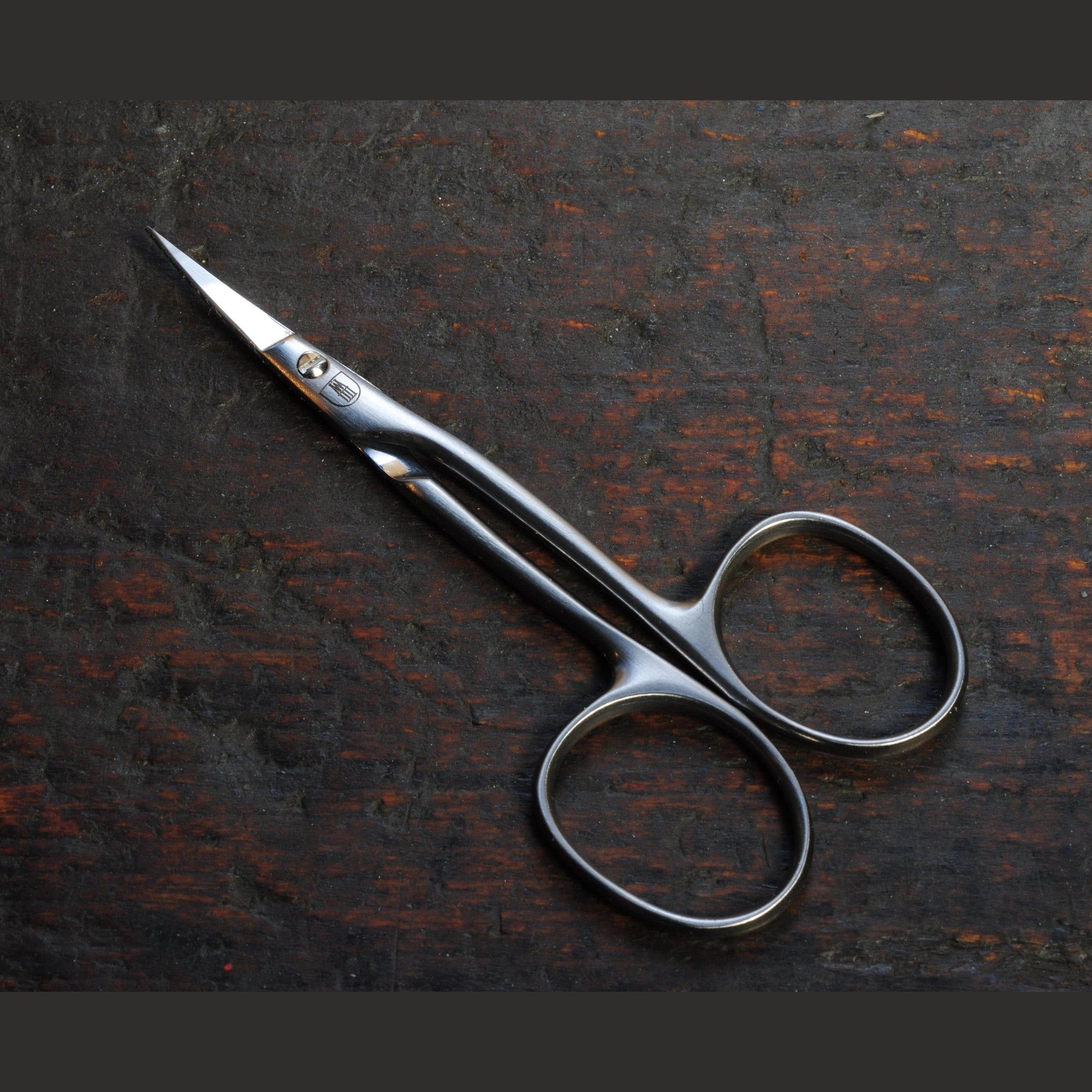 Nagelhautschere aus Metall, auf dunklem Holz. Scharfe, gebogene Klingen und runde Griffe.