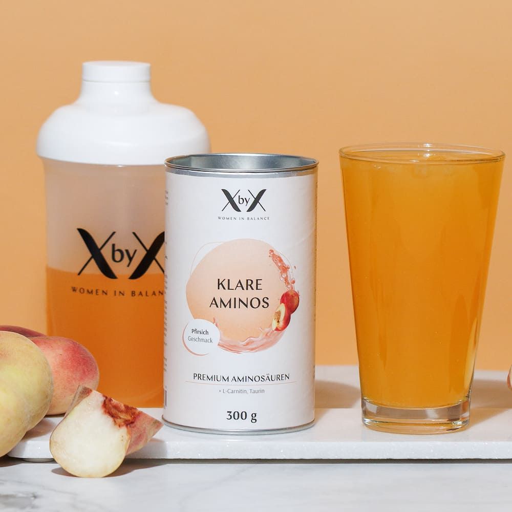 Produkt-Arrangement mit Dose, Shaker, Glas Flüssigkeit und Pfirsichen. Dose mit "XbyX" und "Klare Aminos".