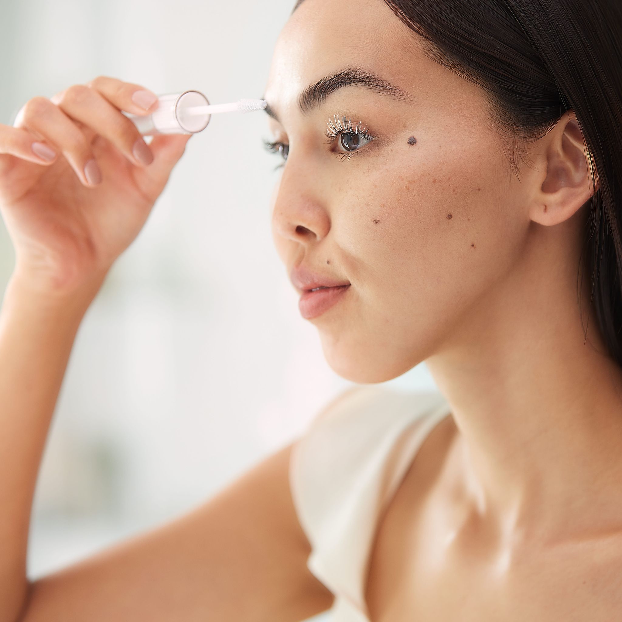 Frau trägt Wimpern- und Augenbrauenmaske mit Applikator auf.