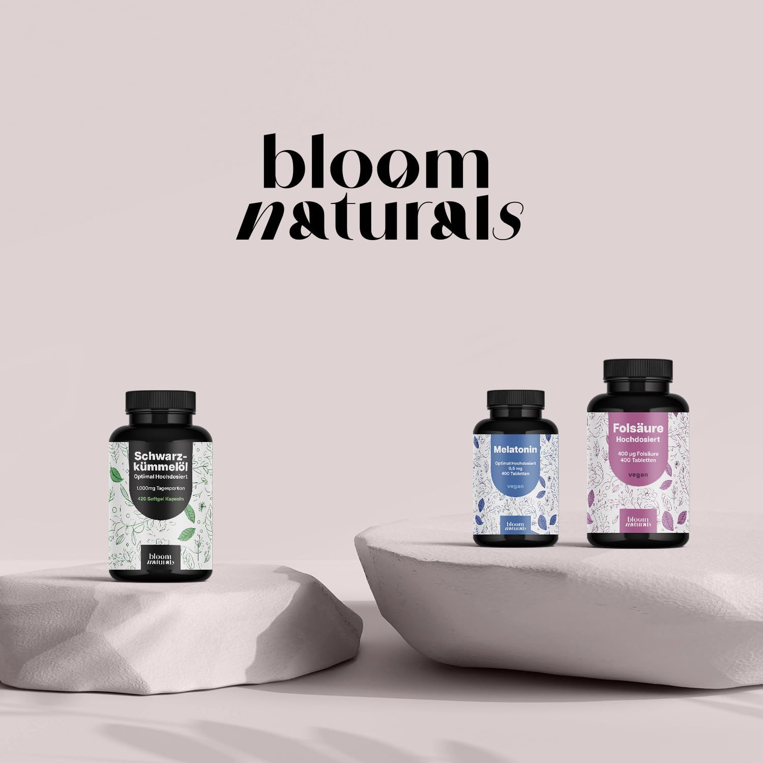 Drei Flaschen: Schwarzkümmelöl, Melatonin, Folsäure. Bloom Naturals Logo. Auf Podesten platziert.