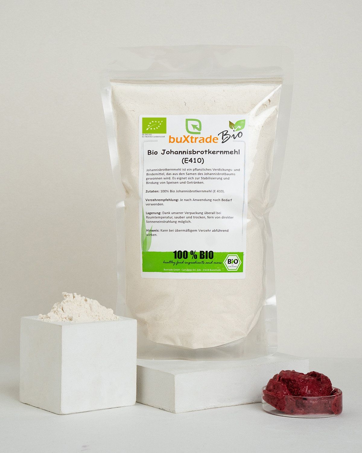 Bio Johannisbrotkernmehl (E410) in einem Standbodenbeutel mit Etikett, daneben ein Würfel mit Mehl und eine Eistüte mit Beeren.