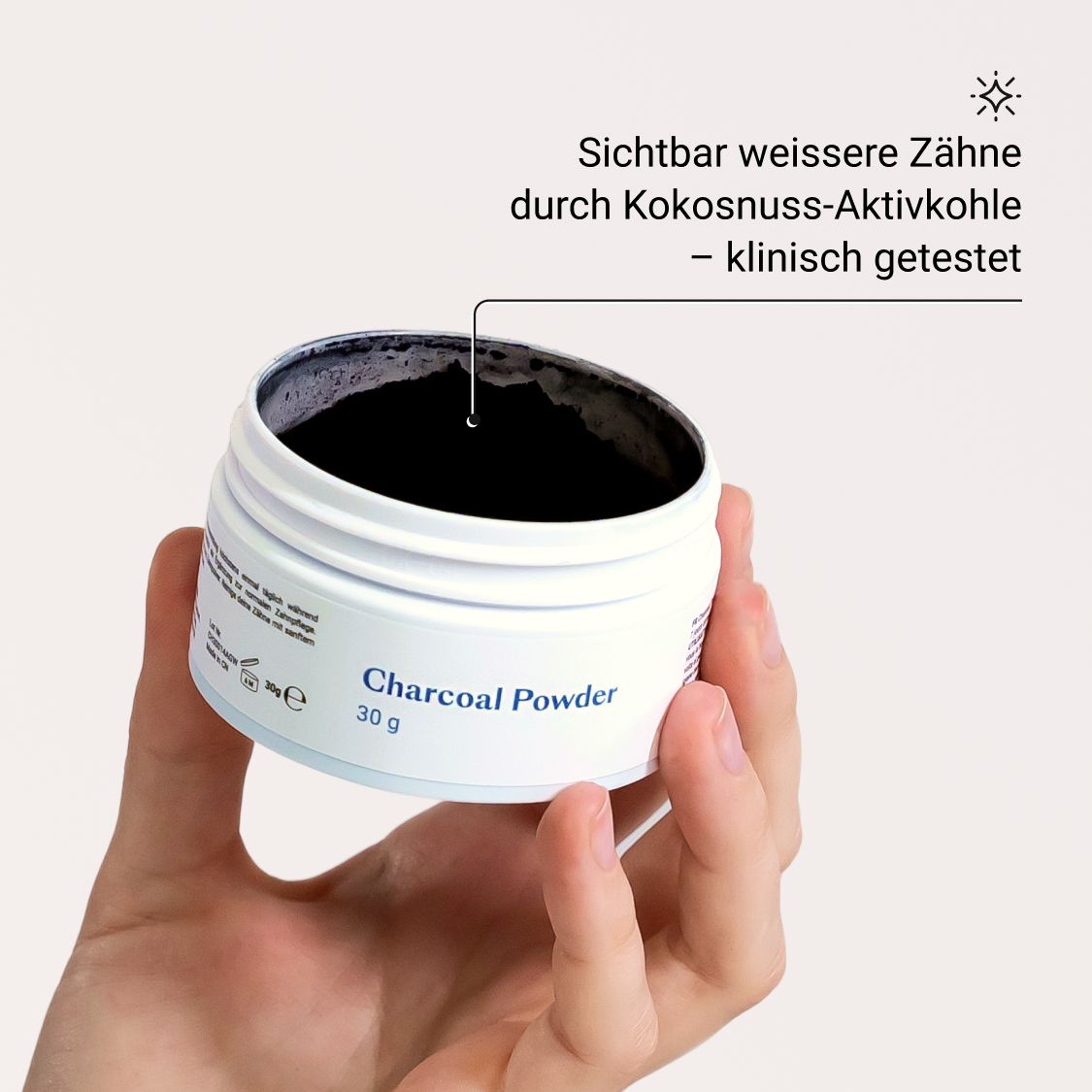 Hand hält Dose mit schwarzem Pulver. Text: Charcoal Powder, 30 g. Sichtbar weißere Zähne.