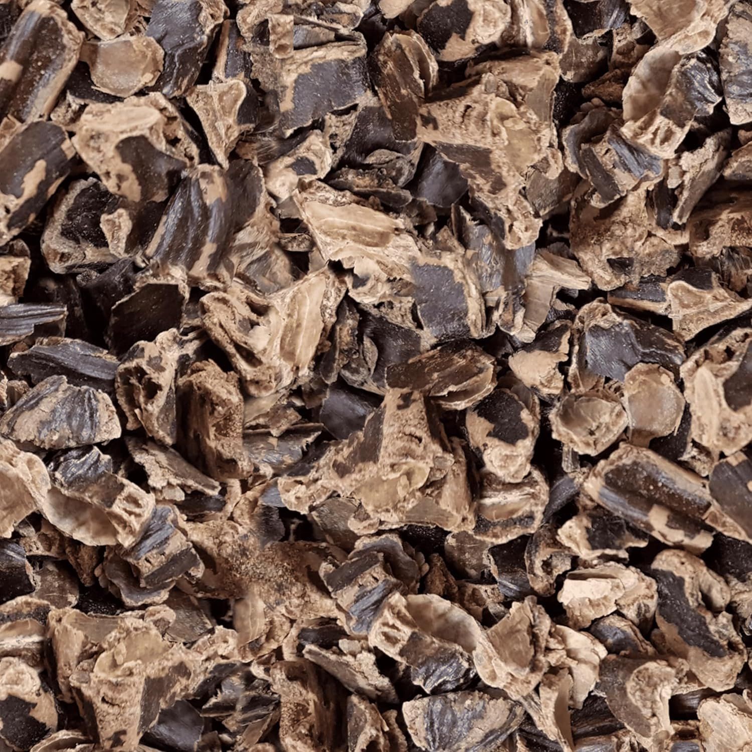 Nahaufnahme von zerkleinerten, braunen Johannisbrot-Schoten. Die Stücke sind unregelmäßig geformt und von unterschiedlicher Größe.