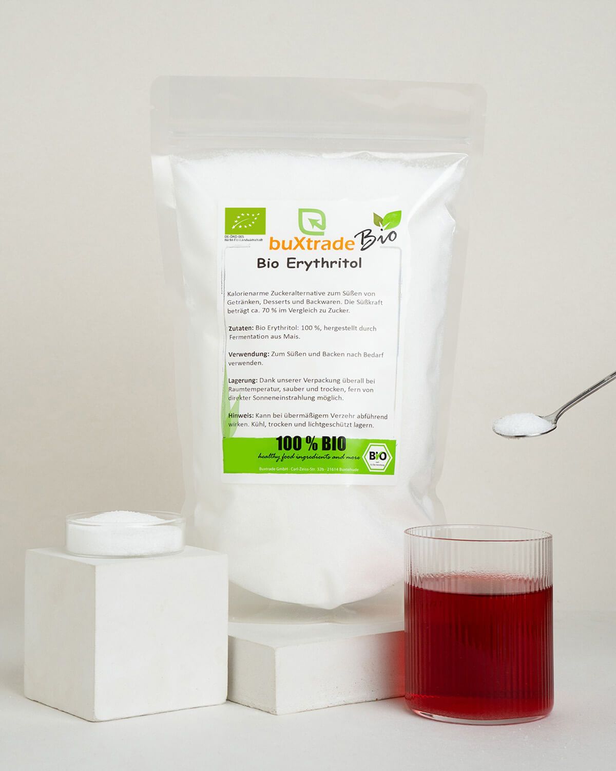 Bio Erythritol Pulver neben einem Glas rotem Getränk, einem Löffel mit Erythritol und einem weißen Würfel.