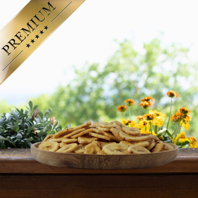 Getrocknete Bananenscheiben in Holzschale auf Tisch. Banner: 'PREMIUM'. Hintergrund: Garten mit Blumen.