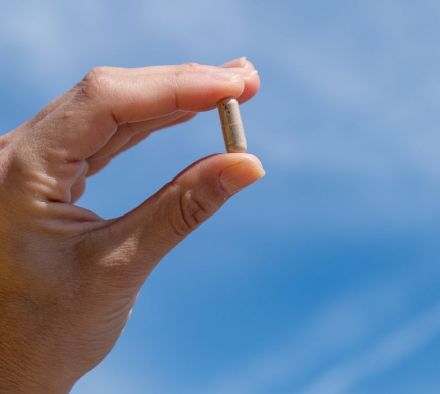 Finger halten eine einzelne Kapsel des Biotin Komplex Nahrungsergänzungsmittels vor blauem Himmel.