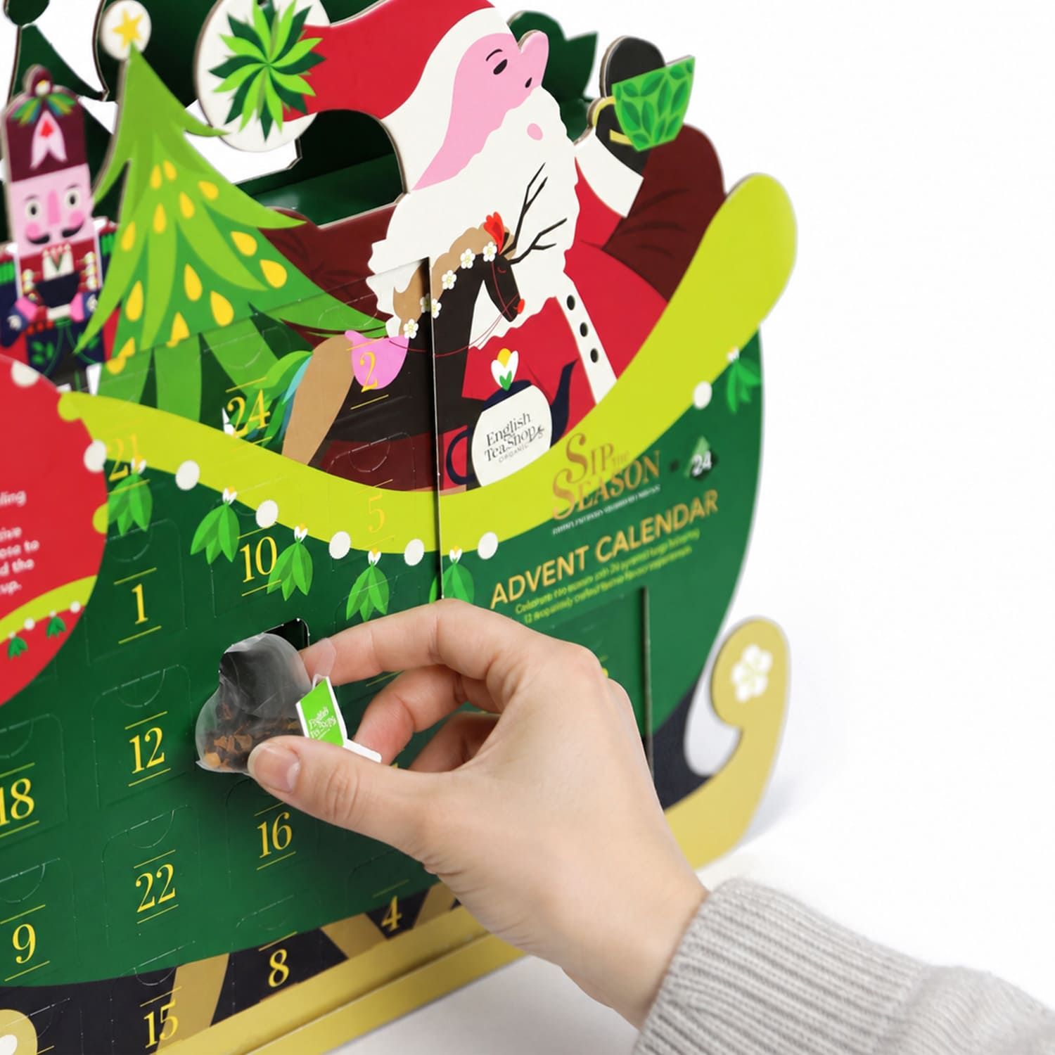 Hand entnimmt Teebeutel aus Adventskalender in Schlittenform. Kalender mit Nikolaus-Motiv und 24 Türchen.