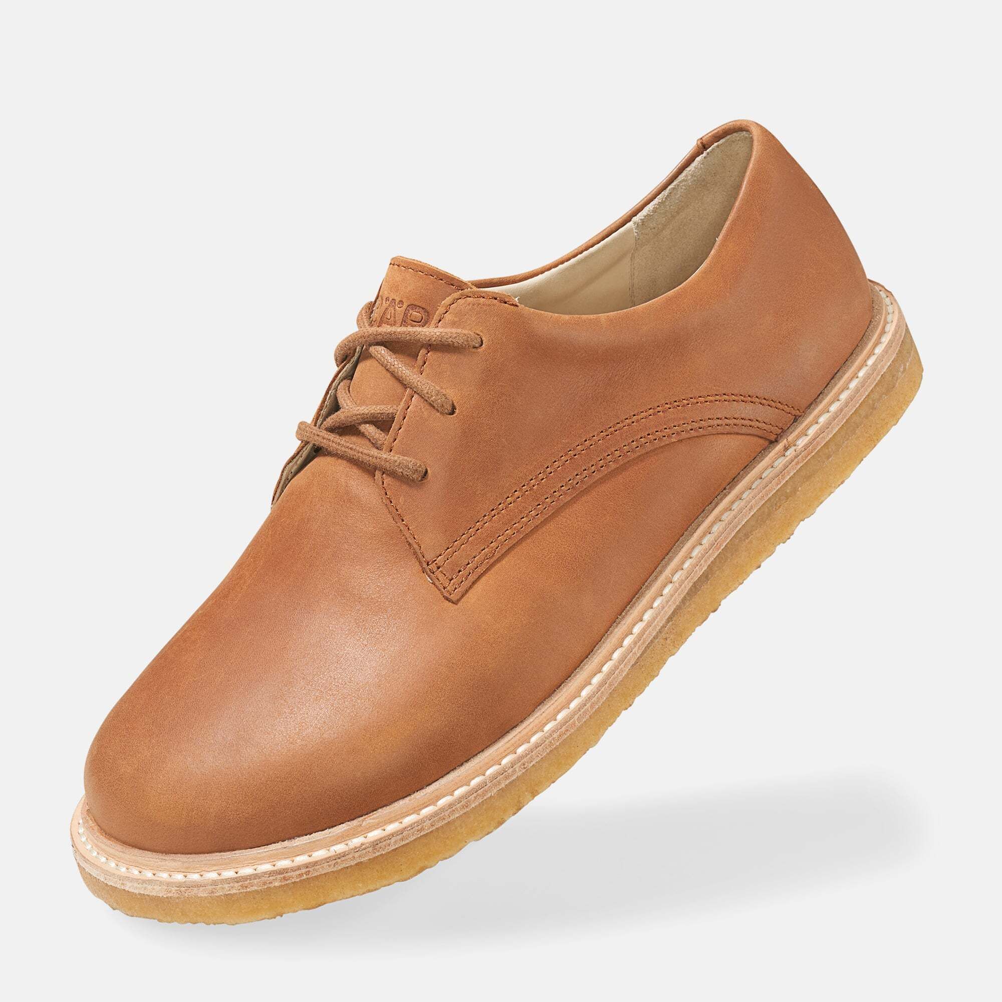 Brauner Lederschnürschuh. Runde Zehe, helle Sohle. Schnürsenkel. Schuh leicht von unten gesehen.