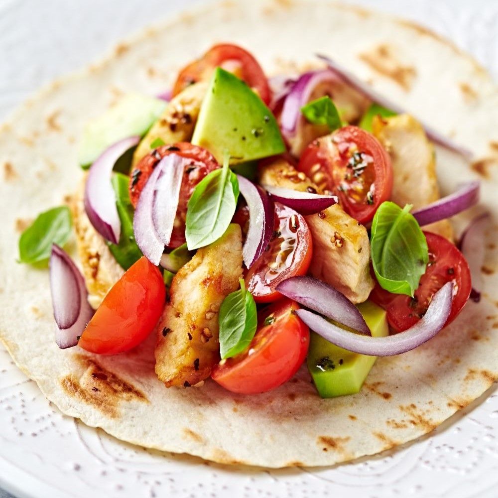 Tortilla mit Hähnchen, Tomaten, Avocado, Zwiebeln und Basilikum. Draufsicht. Auf hellem Untergrund.