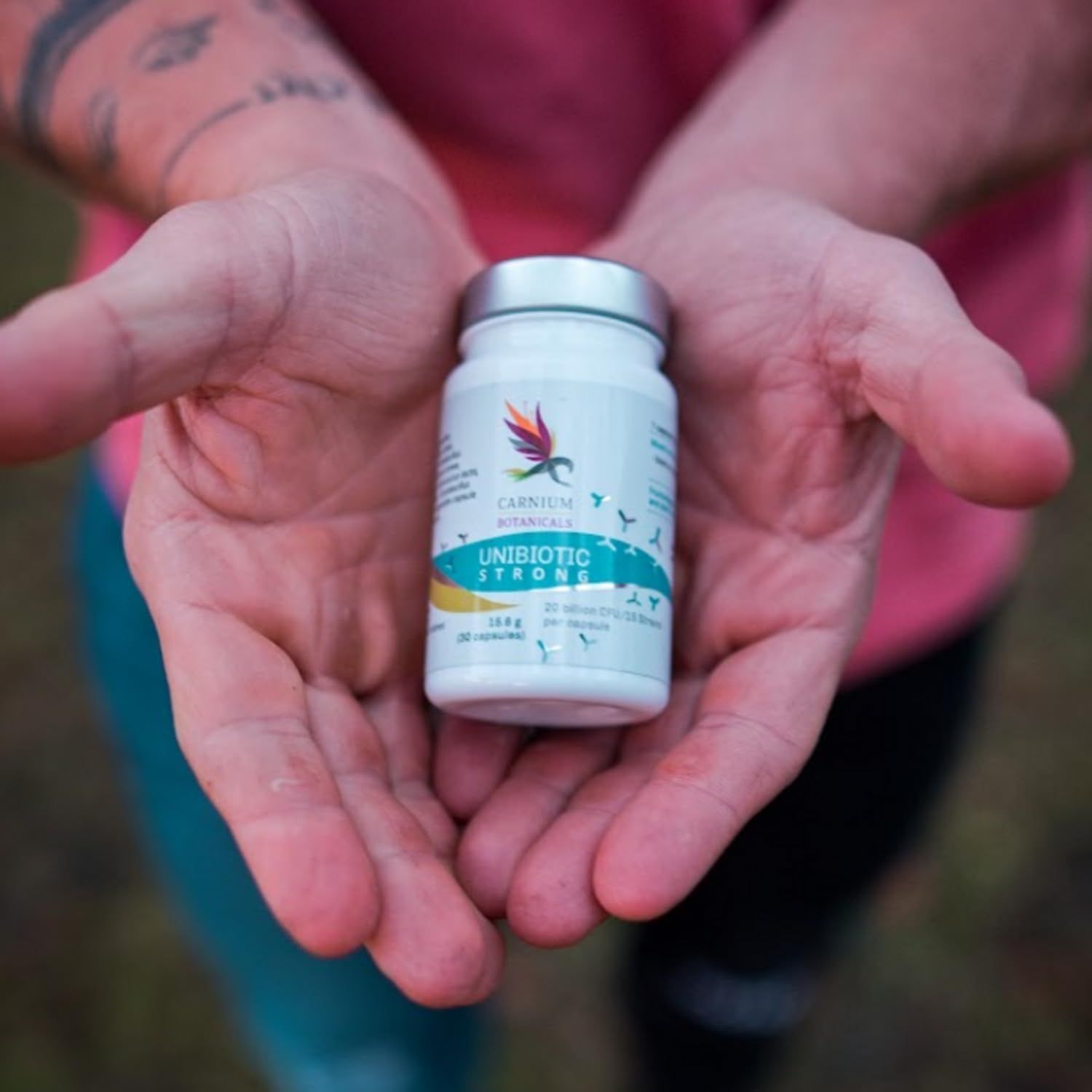Flasche mit Kapseln in Händen. Aufschrift: Unibiotic STRONG, 20 Milliarden CFU/15 Stämme. Marke: CARNIUM BOTANICALS.
