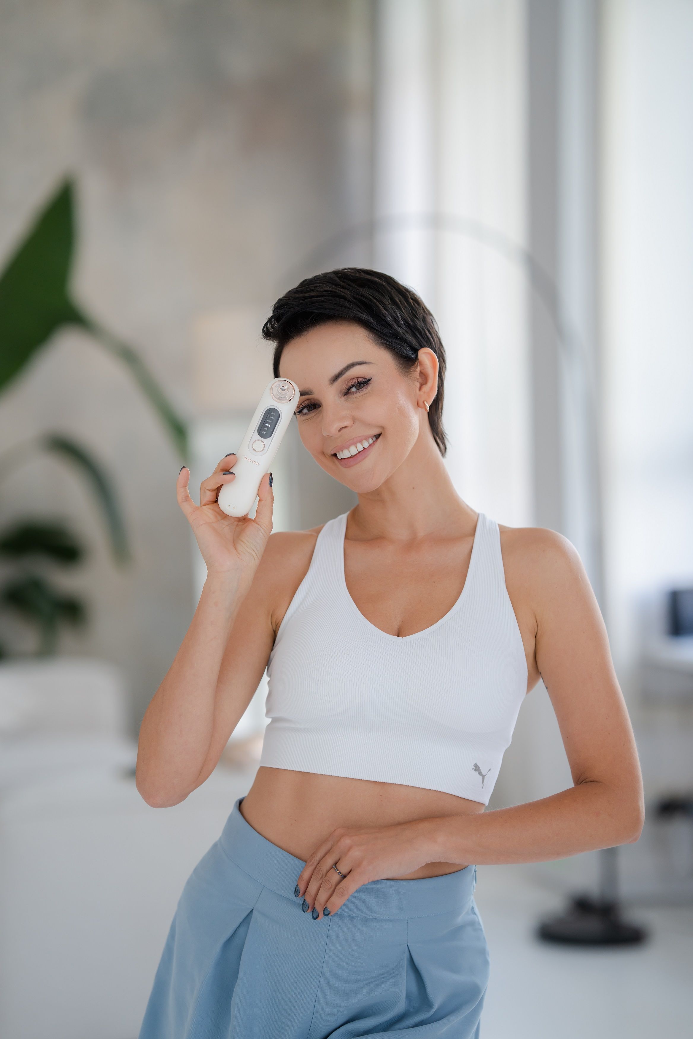 Frau hält BEAUTIFLY B-Derma Glow Diamant Mikrodermabrasion-Gerät. Weiß, mit Bedienfeld.