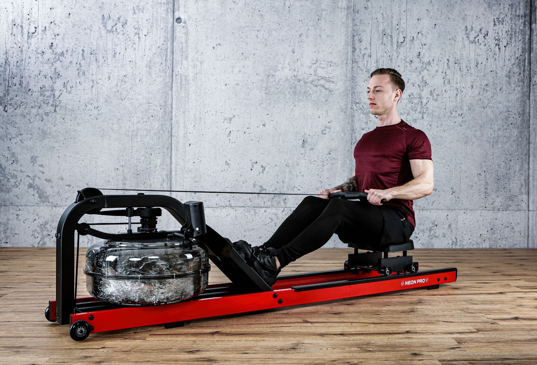 Mann rudert auf einem roten und schwarzen Rudergerät. FUEL Fitness RG700. Wasserbehälter, Sitz, Fußstützen.