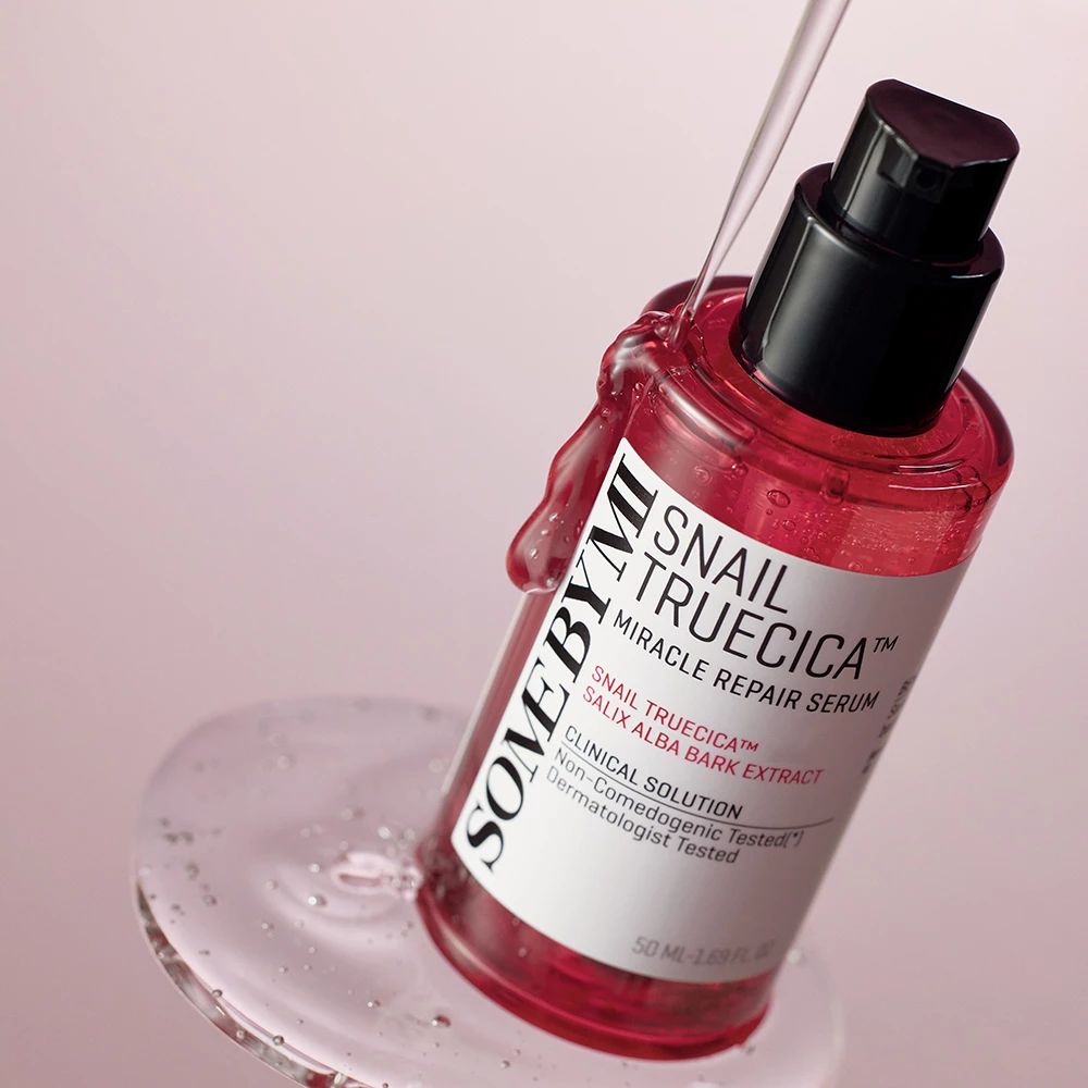 Rotes Serumfläschchen mit schwarzem Pumpverschluss. Produktname und Inhaltsstoffe auf dem Etikett. Flüssigkeit tropft aus der Flasche.