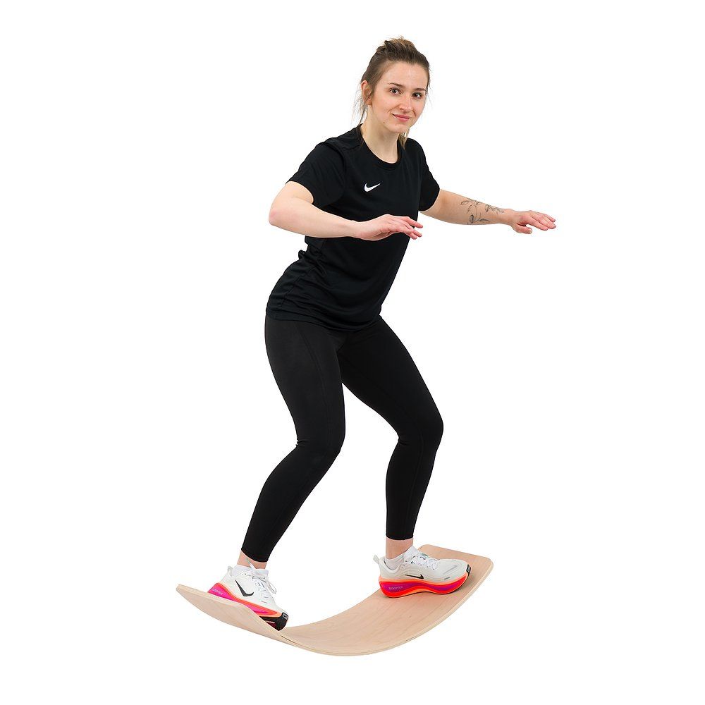 Frau steht auf einem gebogenen Balance Board, Arme seitlich ausgestreckt.