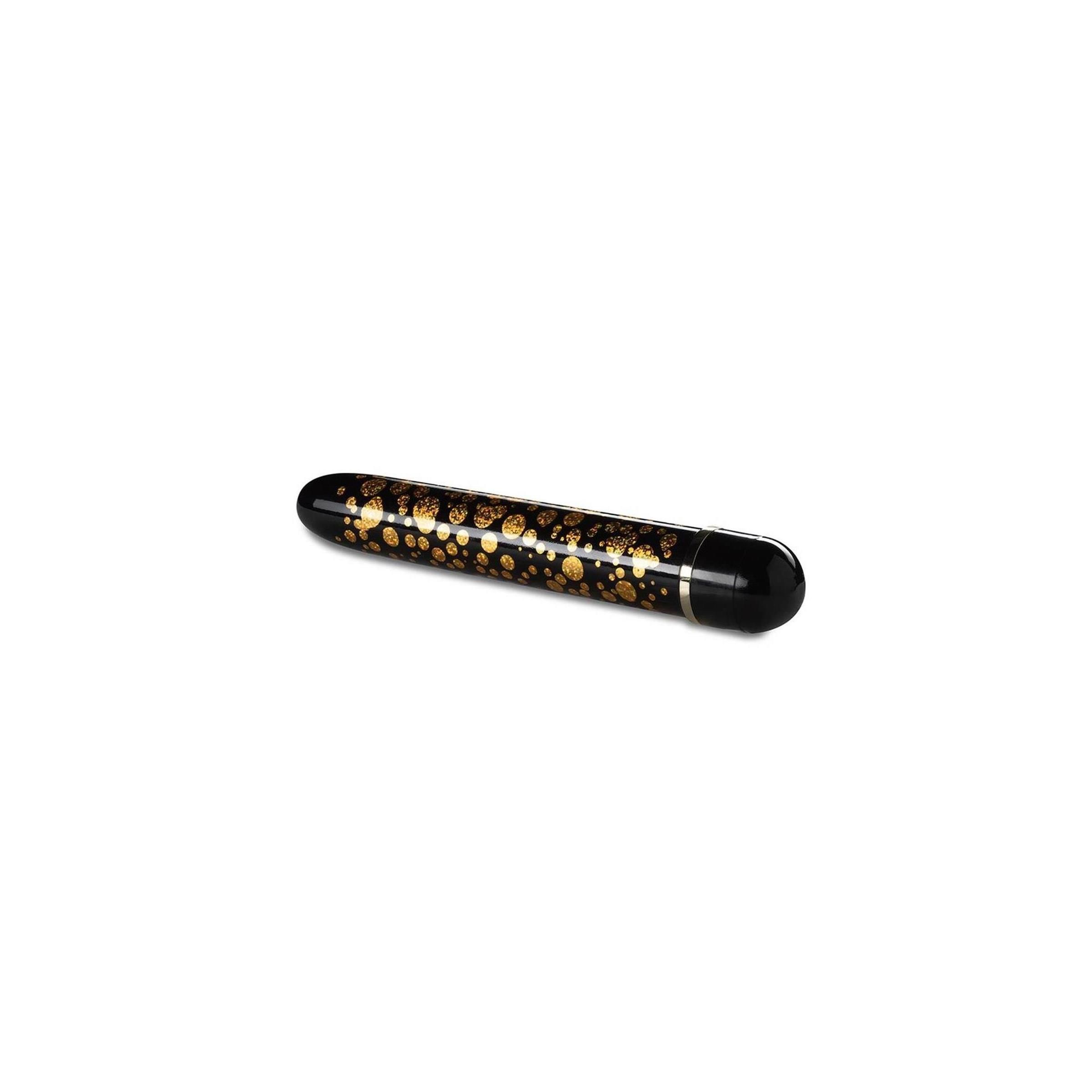 Schwarzer Vibrator mit goldenen Punkten. Zylindrische Form, abgerundete Enden. Schwarzer Sockel.