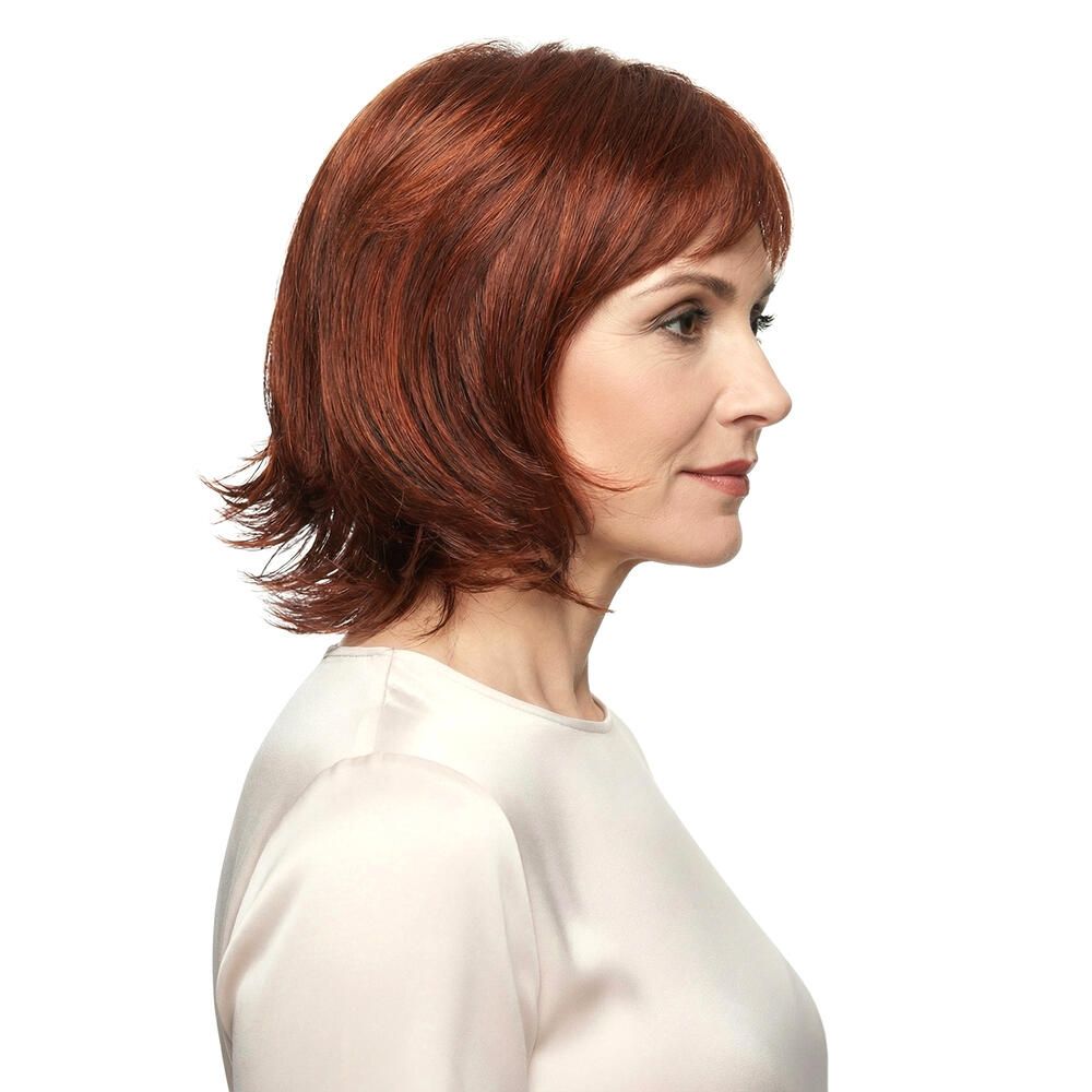 Frau mit roter Perücke MAILAND. Seitenansicht. Kurzes, gewelltes Haar. Trägt ein cremefarbenes Oberteil. Blick nach rechts.