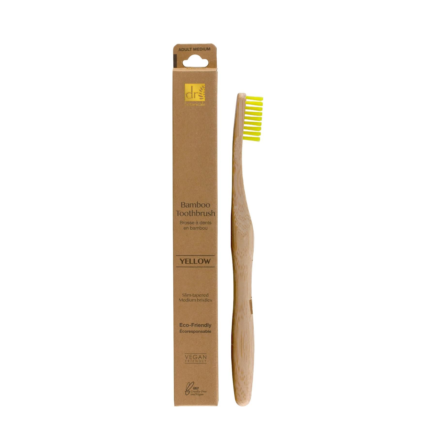 Dr. Botanicals Bambuszahnbürste Gelb mit gelben Borsten und Bambusgriff, neben der Verpackung.