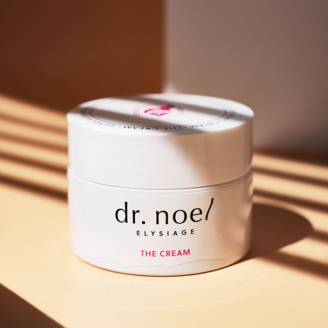 Weißes Creme-Glas mit 'dr. noel/ ELYSIAGE THE CREAM' Aufschrift. Schatteneffekt.